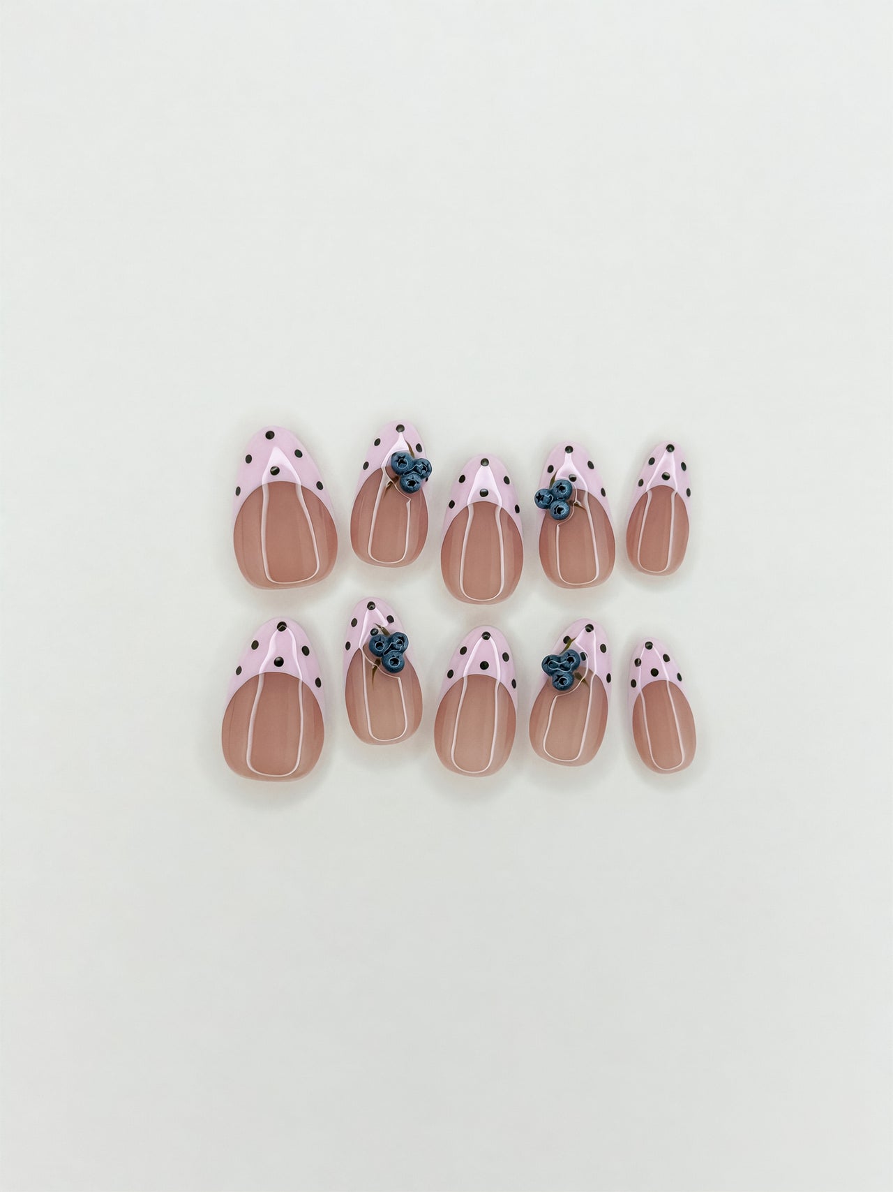 Blueberry Pie handmade reusable press-on nails laid flat, featuring sheer nude bases, pale pink polka dot French tips and raised 3D blueberry nail art in a short almond shape.