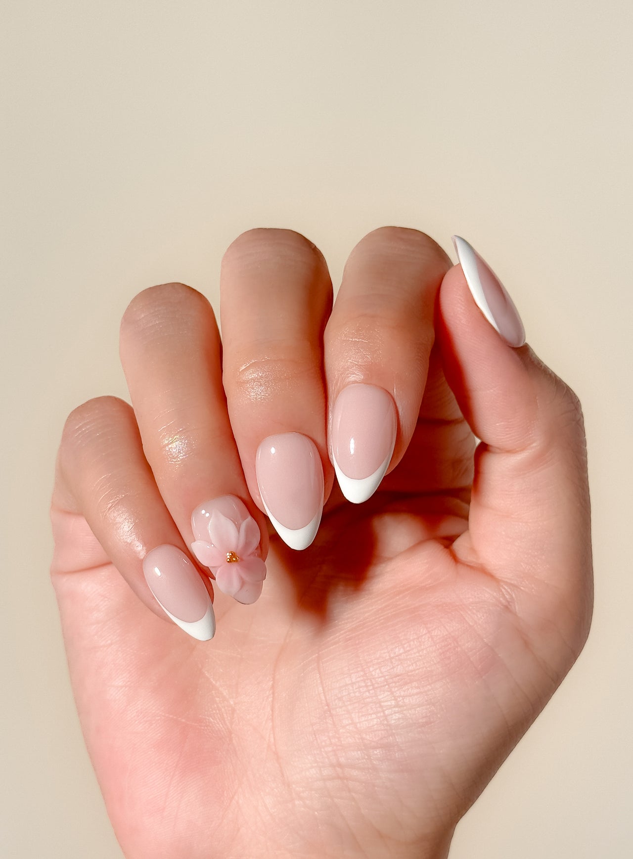 White French tip press-on nails with delicate 3D floral detailing in a glossy medium almond shape. Handmade reusable false nails with a sheer nude pink base inspired by romantic bridal nails, soft feminine manicures and elevated floral French tip designs.