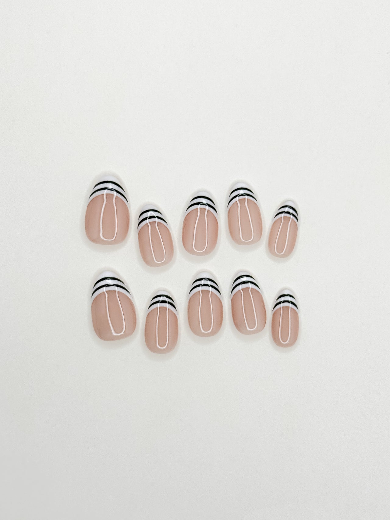 Black and white striped French tip press-on nails in a glossy short almond shape with a sheer nude base. Handmade reusable false nails inspired by graphic French manicure styles, Y2K glam nails and monochrome minimalist nail art.