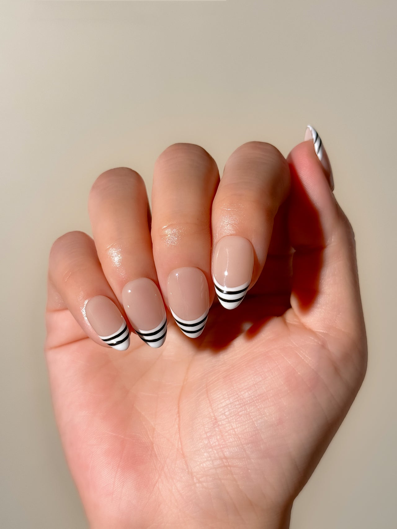 Black and white striped French tip press-on nails in a glossy short almond shape with a sheer nude base. Handmade reusable false nails inspired by graphic French manicure styles, Y2K glam nails and monochrome minimalist nail art.