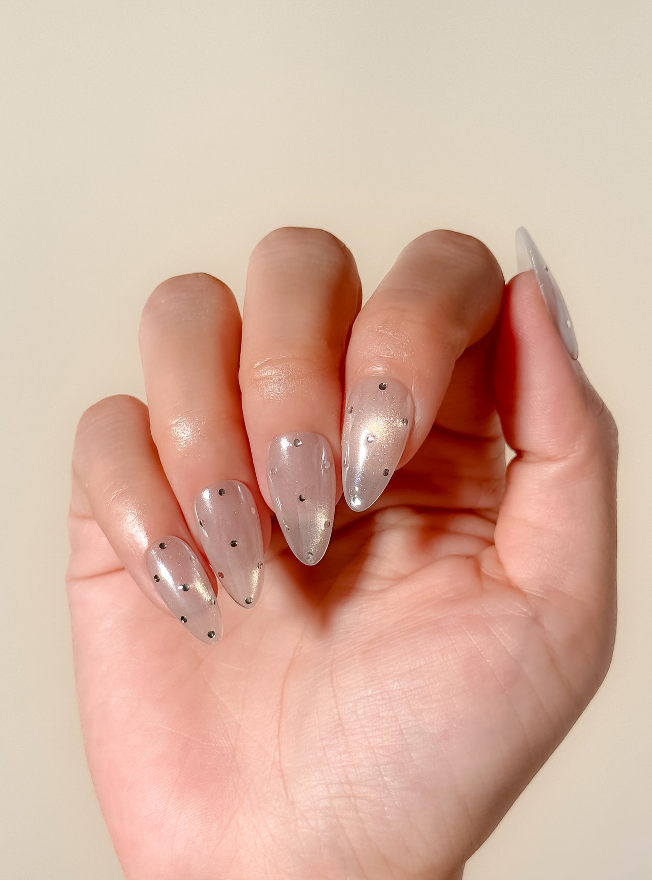 Moon Sugar handmade reusable press-on nails laid flat, featuring a sheer champagne cat-eye finish, soft nude shimmer and tiny silver dot nail art in a medium almond shape.
