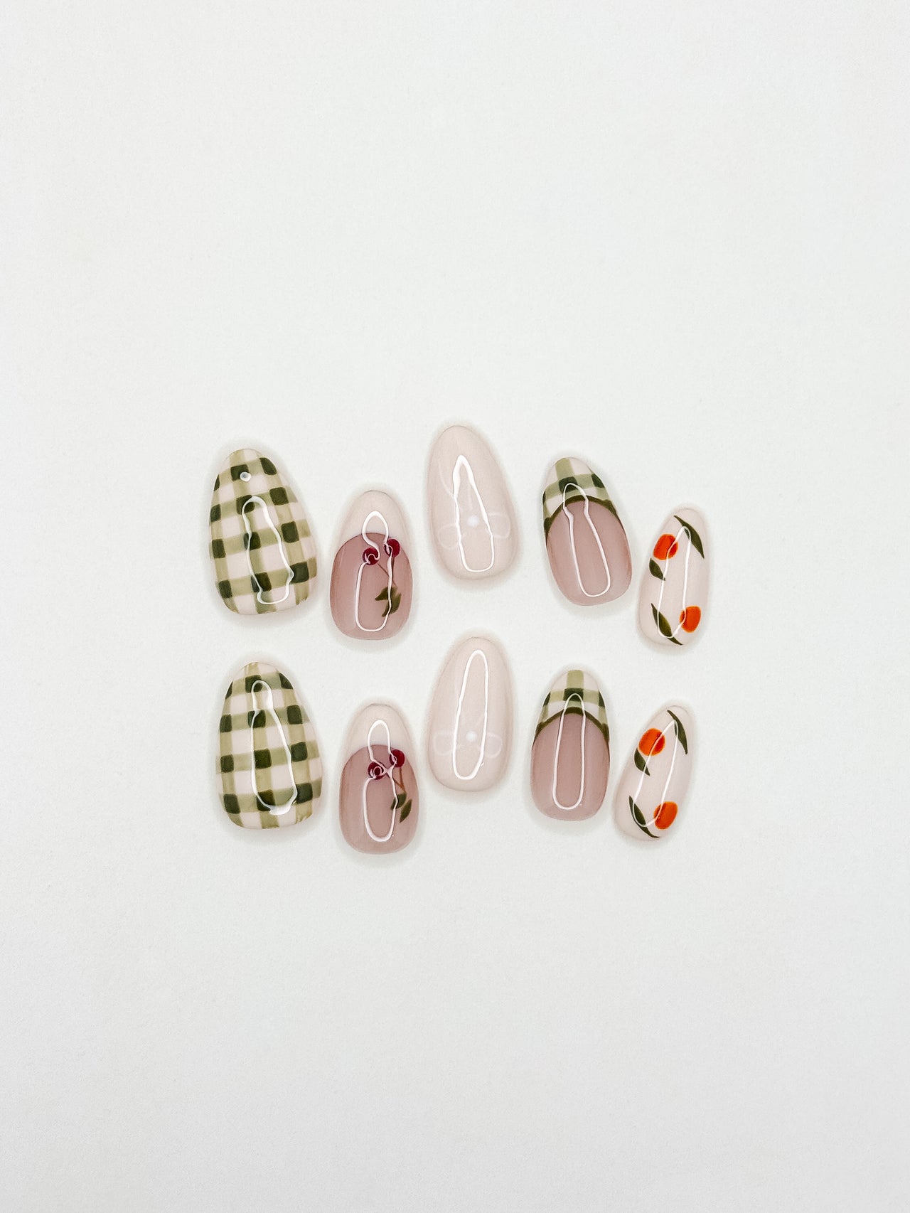 Cream and olive green press-on nails with hand-painted cherry, citrus and gingham French tip detailing in a medium almond shape. Handmade reusable false nails inspired by picnic aesthetics, European summer styling and vintage fruit nail art.