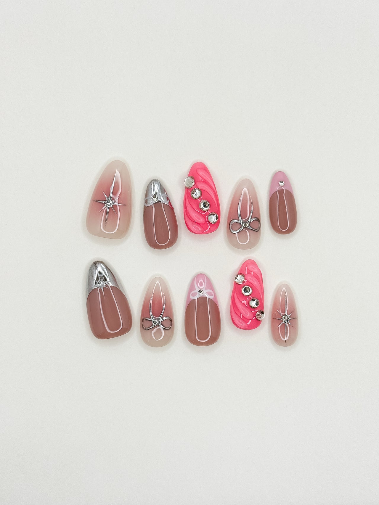 Starlit handmade reusable press-on nails laid flat, featuring sheer nude bases, silver chrome bow details, starburst nail art, hot pink sculpted accents and crystal gems in a medium almond shape.