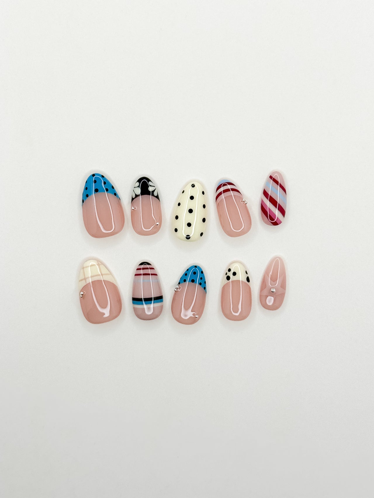 Stripe Club handmade reusable press-on nails laid flat, featuring striped nail art, polka dot French tips, soft nude bases and glossy short almond shapes.