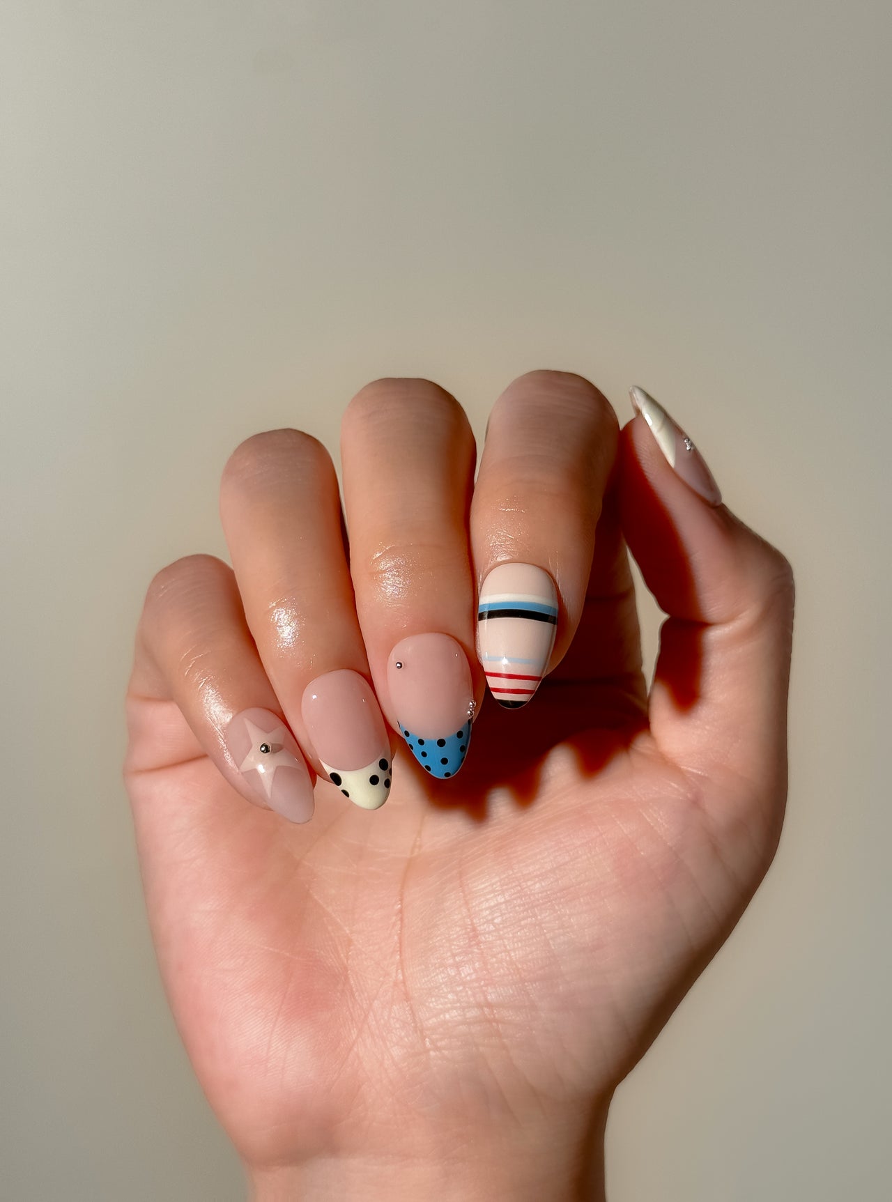 Stripe Club handmade reusable press-on nails laid flat, featuring striped nail art, polka dot French tips, soft nude bases and glossy short almond shapes.