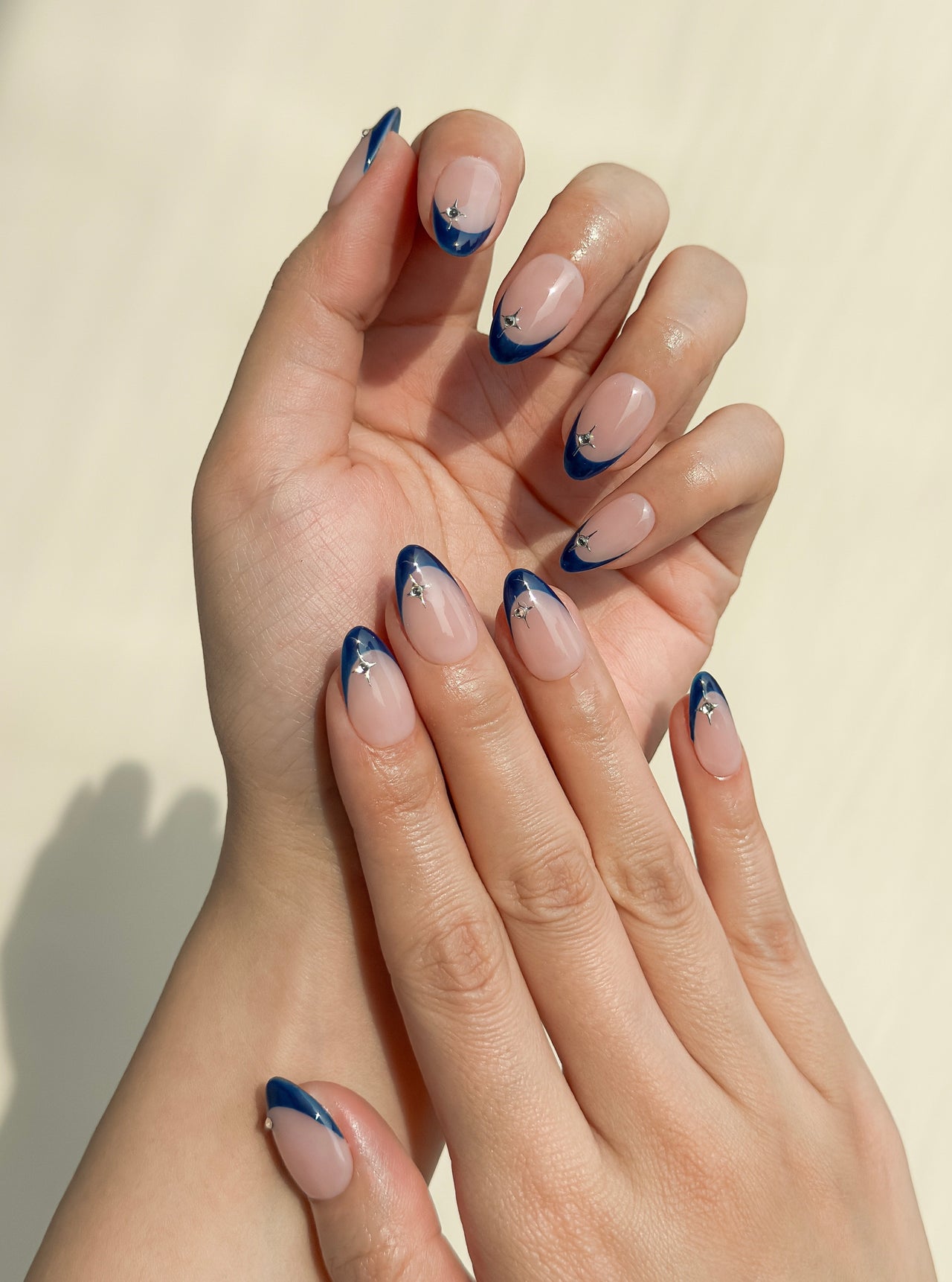 After Midnight handmade press-on nails arranged on a white background, featuring short almond nails with deep navy skinny French tips, a sheer blush base and silver star embellishments.