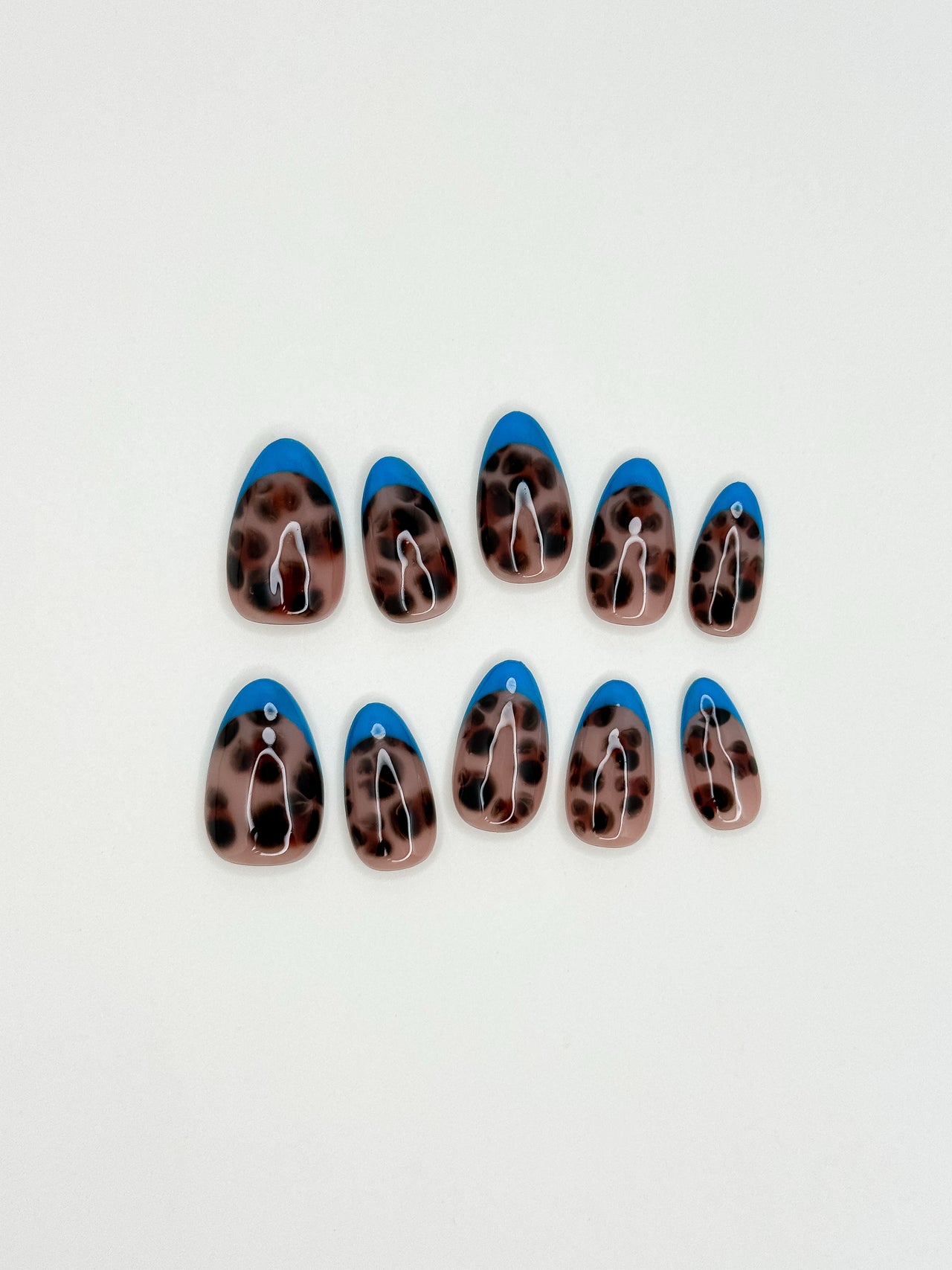 Blue Monday almond-shaped press-on nails arranged in two rows on a plain white background. The nails feature a glossy blue French tip and a brown and black leopard print middle base.