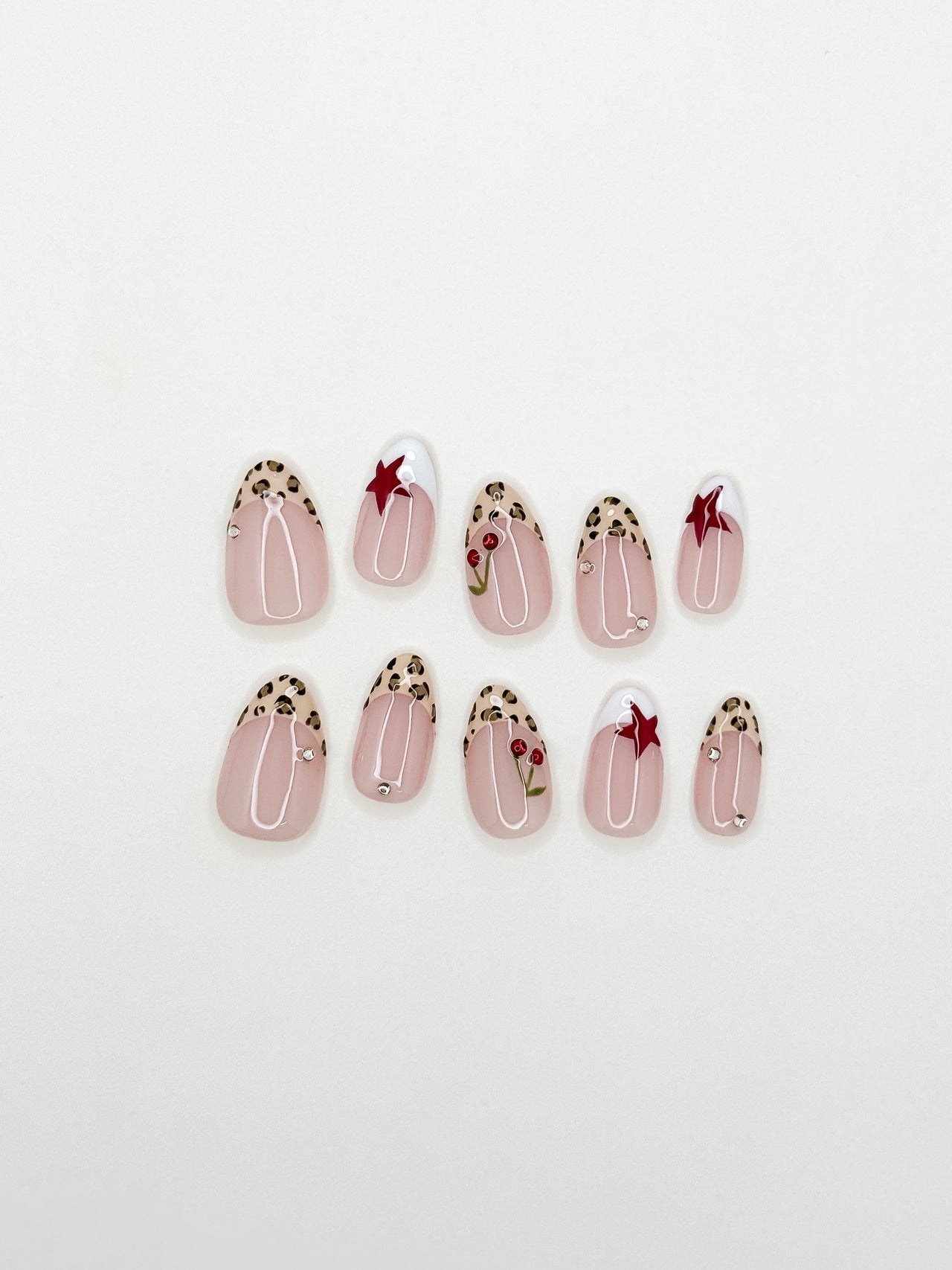 Cherry Bombshell handmade press-on nails arranged on a white background, featuring short almond nails with leopard-print skinny French tips, red cherries, red stars and crystal accents.