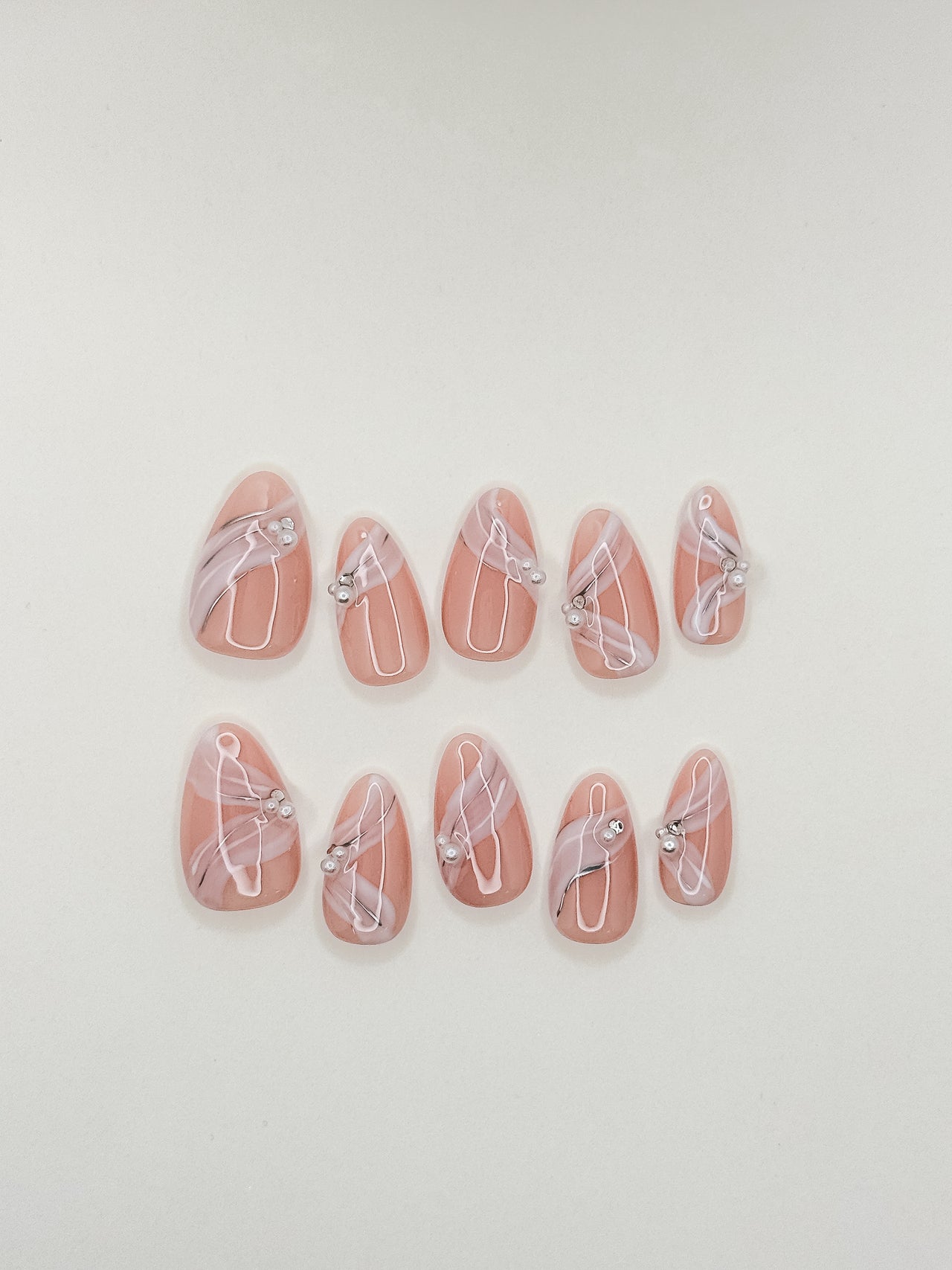 One More Night short almond press-on nails arranged on white, with a sheer blush-nude base, raised white ribbon lines and silver crystals.