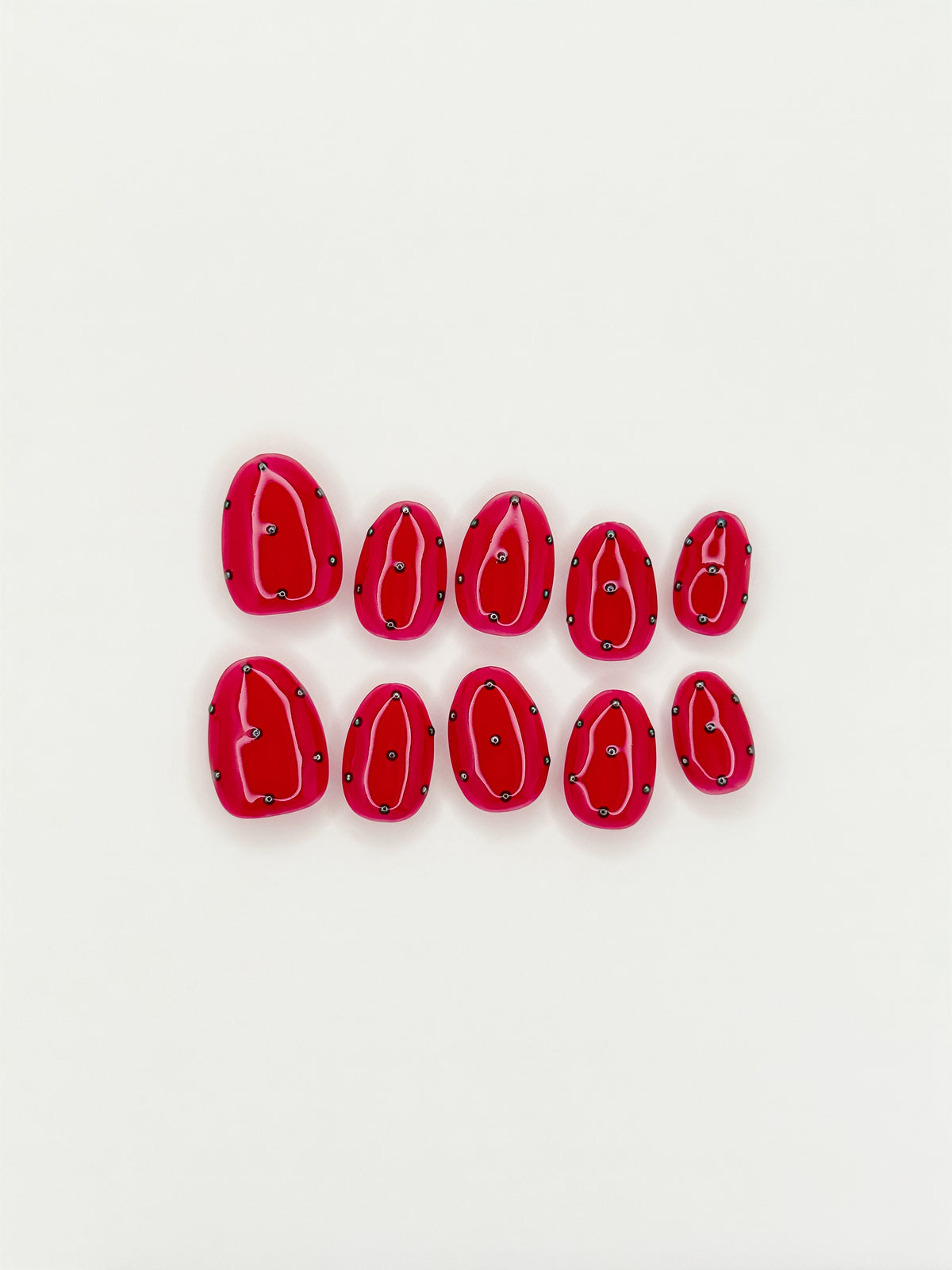 Strike One vivid red extra-short oval press-on nails with silver orbit lines and 3D studs arranged on white.