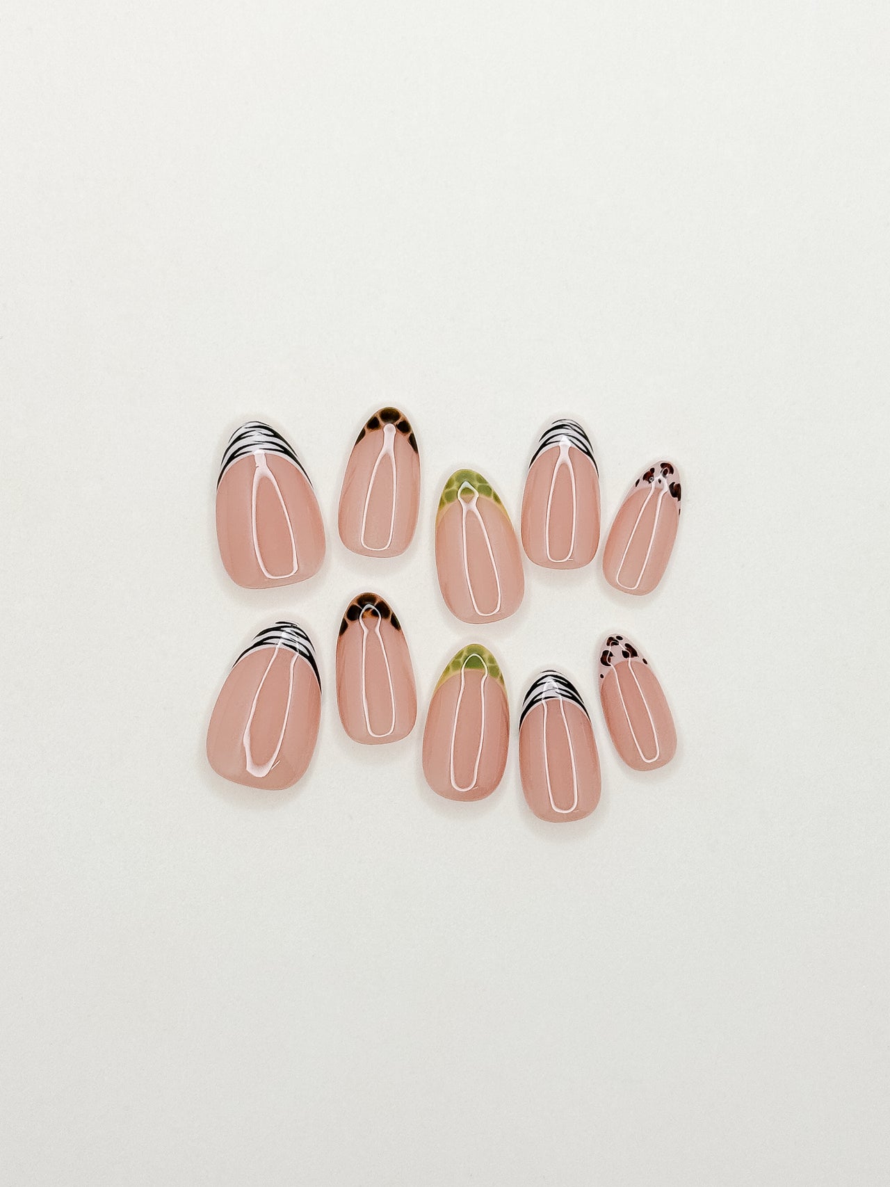 The Wild Card handmade press-on nails arranged on a white background, featuring short almond nails with mixed zebra, tortoiseshell, leopard and green reptile-inspired skinny French tips.