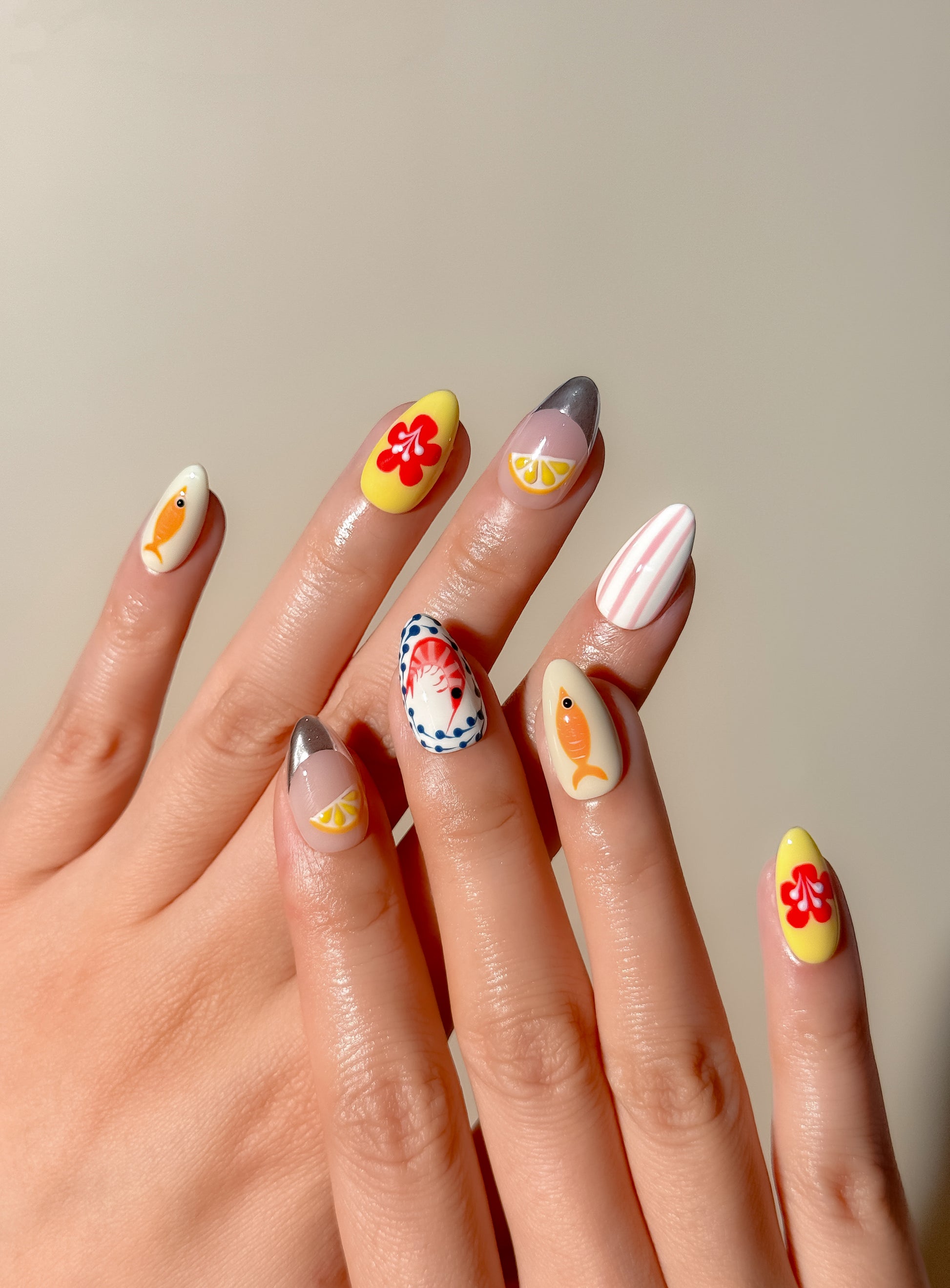 Colourful Mediterranean-inspired press-on nails with hand-painted fish, lemon and floral detailing in a medium almond shape. Handmade reusable false nails inspired by Italian summer holidays, Amalfi Coast aesthetics and playful European resort nail art.