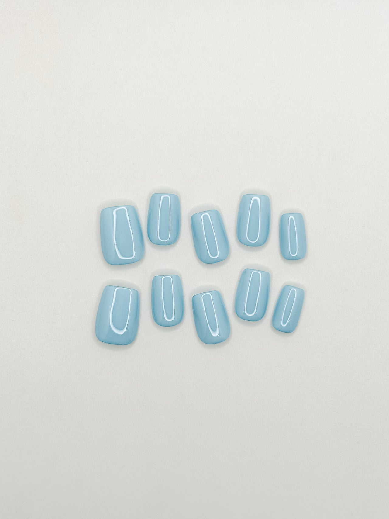 Bluebell handmade reusable press-on nails laid flat, featuring a glossy solid baby blue colour in a short square shape.