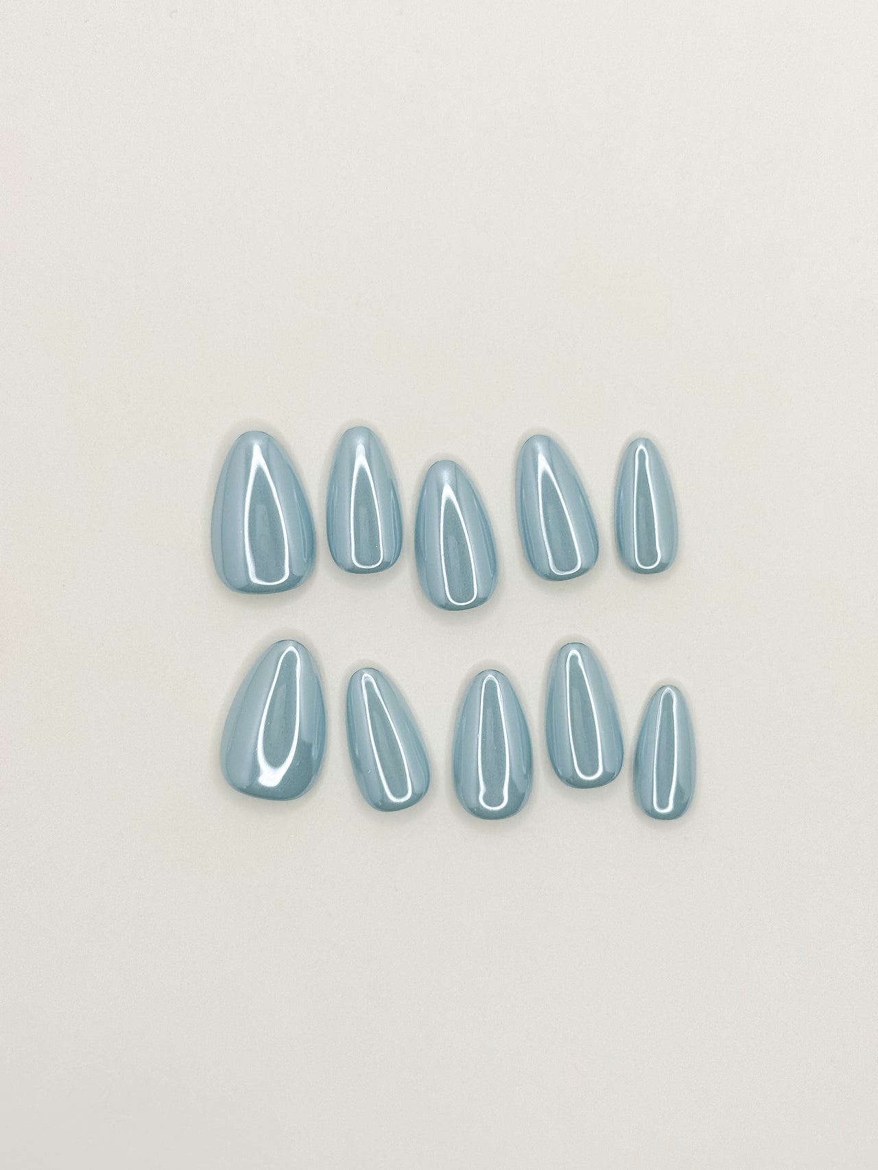 Bluebell Glaze handmade reusable press-on nails laid flat, featuring a soft powder-blue colour, pearly glazed finish and glossy medium almond shape.
