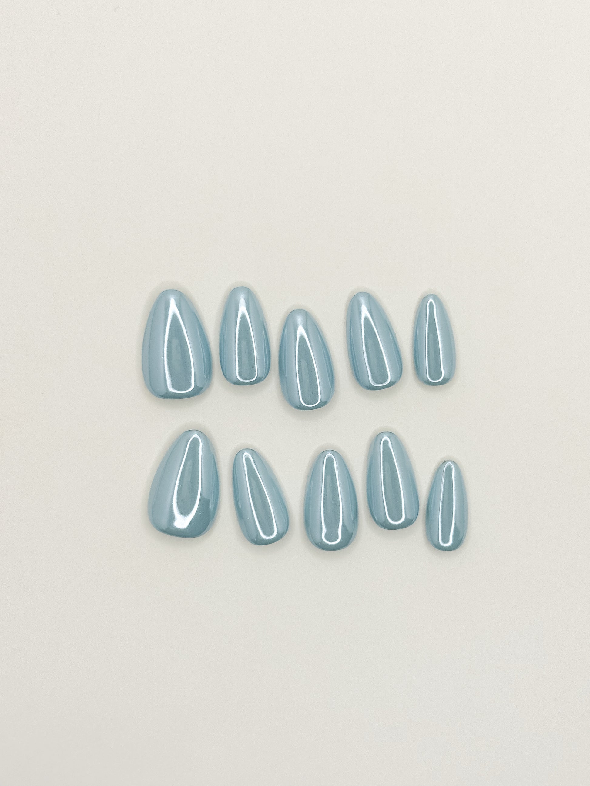 Bluebell Glaze handmade reusable press-on nails laid flat, featuring a soft powder-blue colour, pearly glazed finish and glossy medium almond shape.