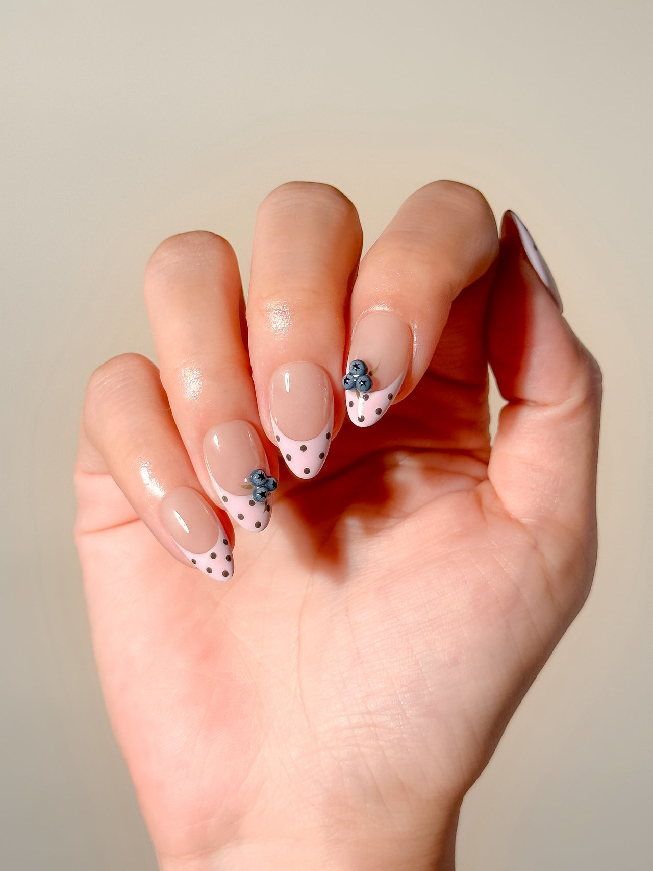 Blueberry Pie handmade reusable press-on nails laid flat, featuring sheer nude bases, pale pink polka dot French tips and raised 3D blueberry nail art in a short almond shape.