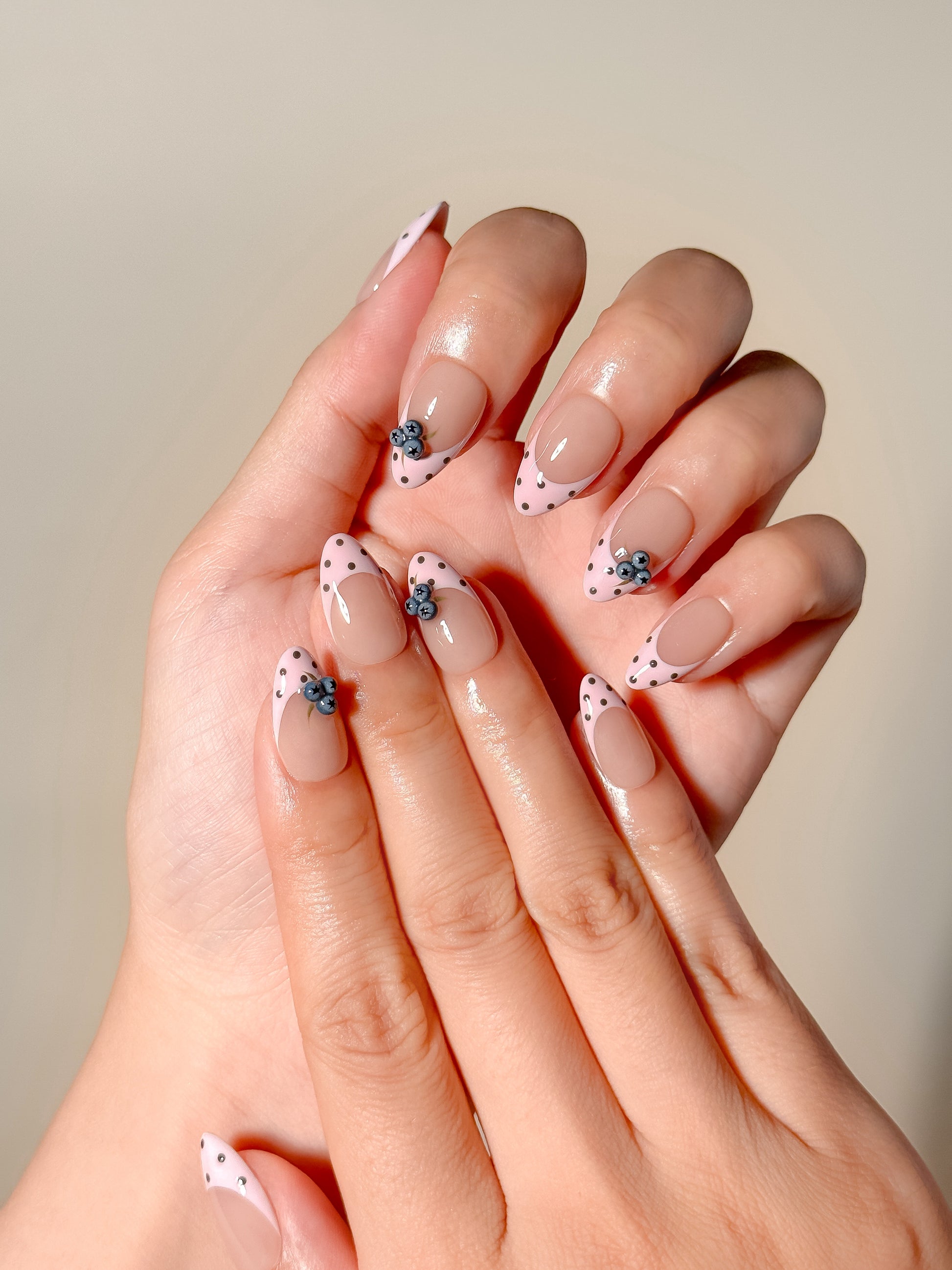 Blueberry Pie handmade press-on nails worn on both hands, showing pink dotted French tips, sheer nude bases and 3D blueberry accents with a glossy short almond finish.