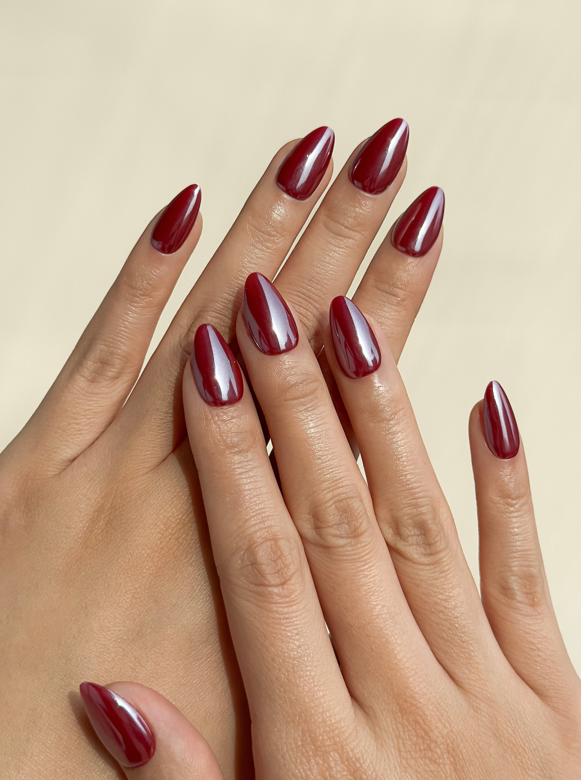 Deep berry red glazed press-on nails in a glossy short almond shape with reflective blackcurrant tones. Handmade reusable false nails inspired by cherry glaze nails, dark red manicures and glossy wine-coloured nail trends.