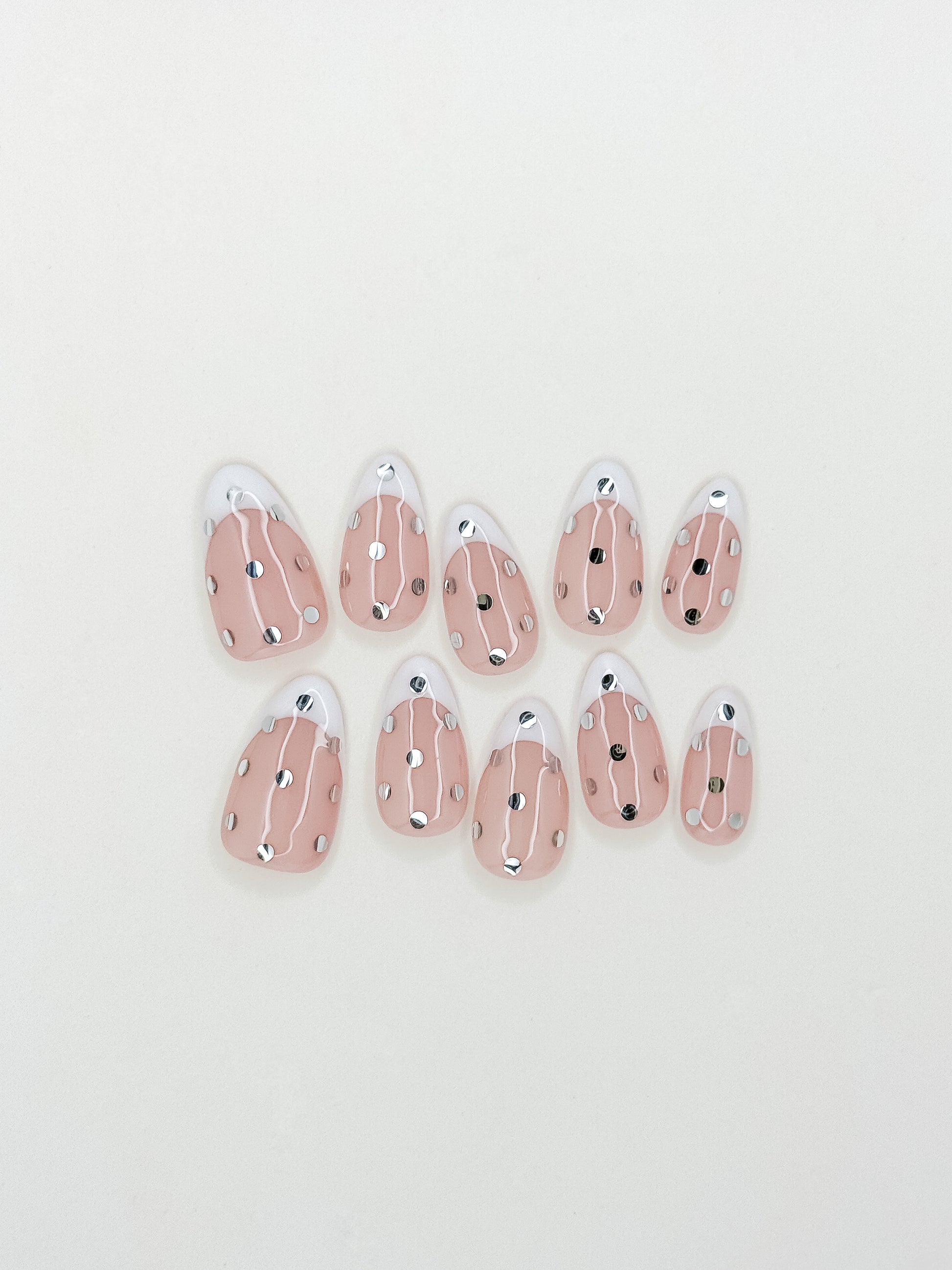 White French tip press-on nails with metallic silver polka dot detailing in a medium almond shape. Handmade reusable false nails inspired by playful French manicures, glossy polka dot nail art and elevated party-ready nail designs.