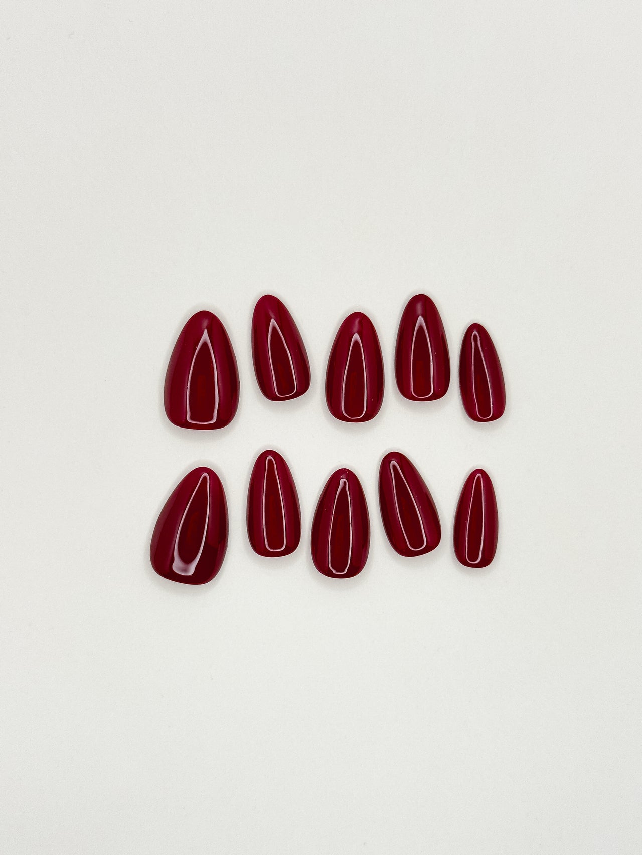 Deep cherry red press-on nails in a glossy short almond shape, featuring a rich burgundy lacquer finish with ultra high shine. Reusable handmade false nails inspired by black cherry, merlot and dark red gel manicure styles, photographed in warm natural lighting.