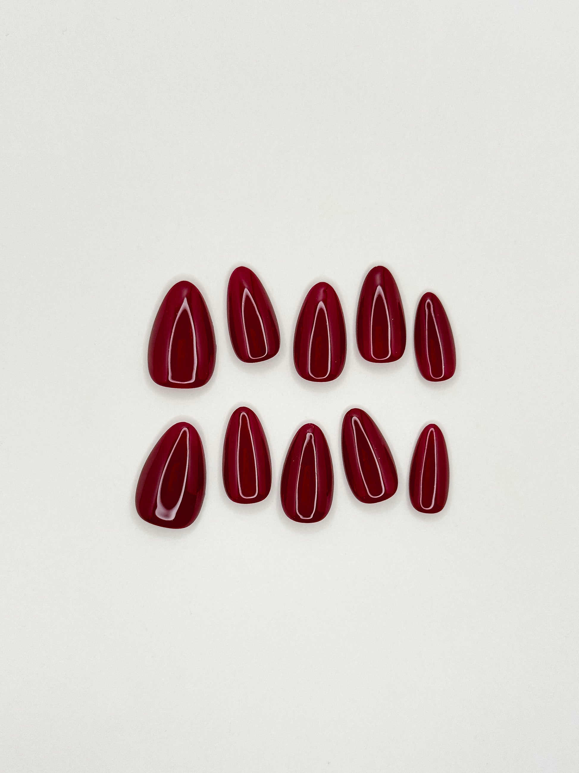 Deep cherry red press-on nails in a glossy short almond shape, featuring a rich burgundy lacquer finish with ultra high shine. Reusable handmade false nails inspired by black cherry, merlot and dark red gel manicure styles, photographed in warm natural lighting.