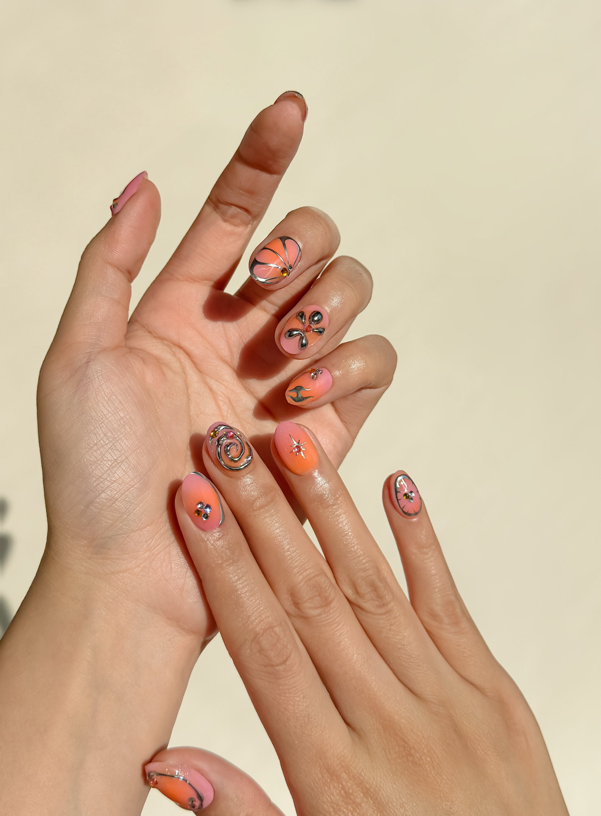 Coral Crush handmade press-on nails on hands, featuring pink and coral gradient tones, metallic chrome accents, playful swirls and floral-inspired statement nail art.