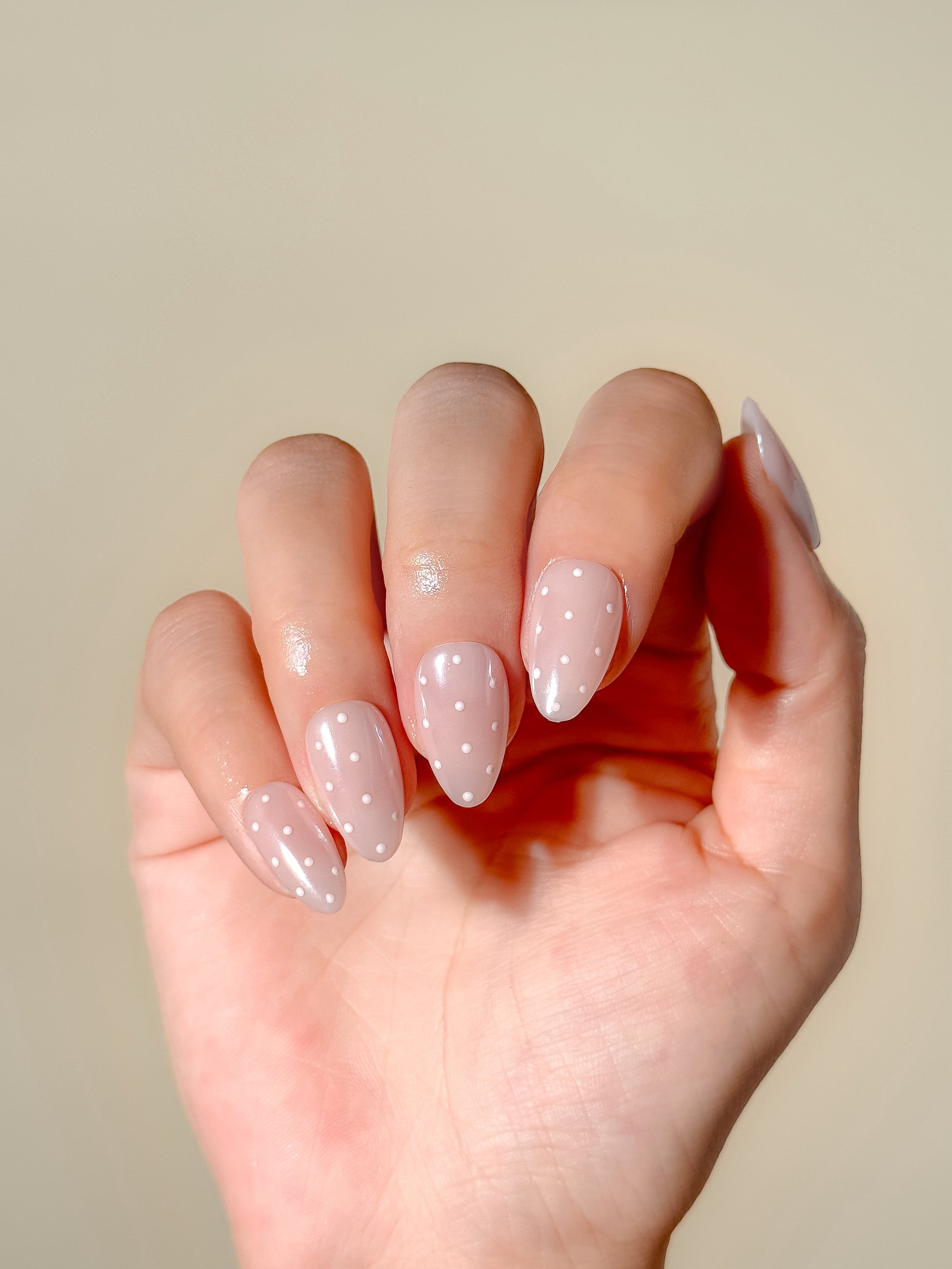 Dottie Glaze sheer pink polka dot press-on nails worn on hand with glossy gel glazed finish and short almond tips