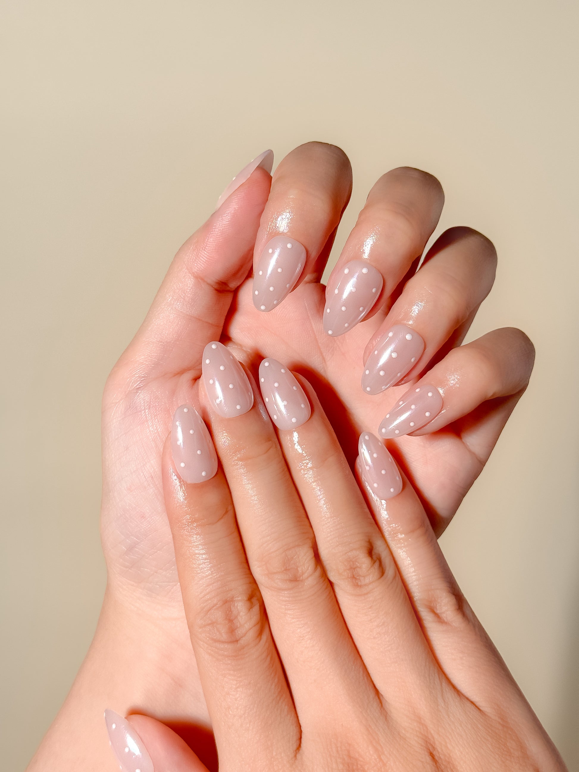 Dottie Glaze sheer pink polka dot press-on nails worn on hand with glossy gel glazed finish and short almond tips
