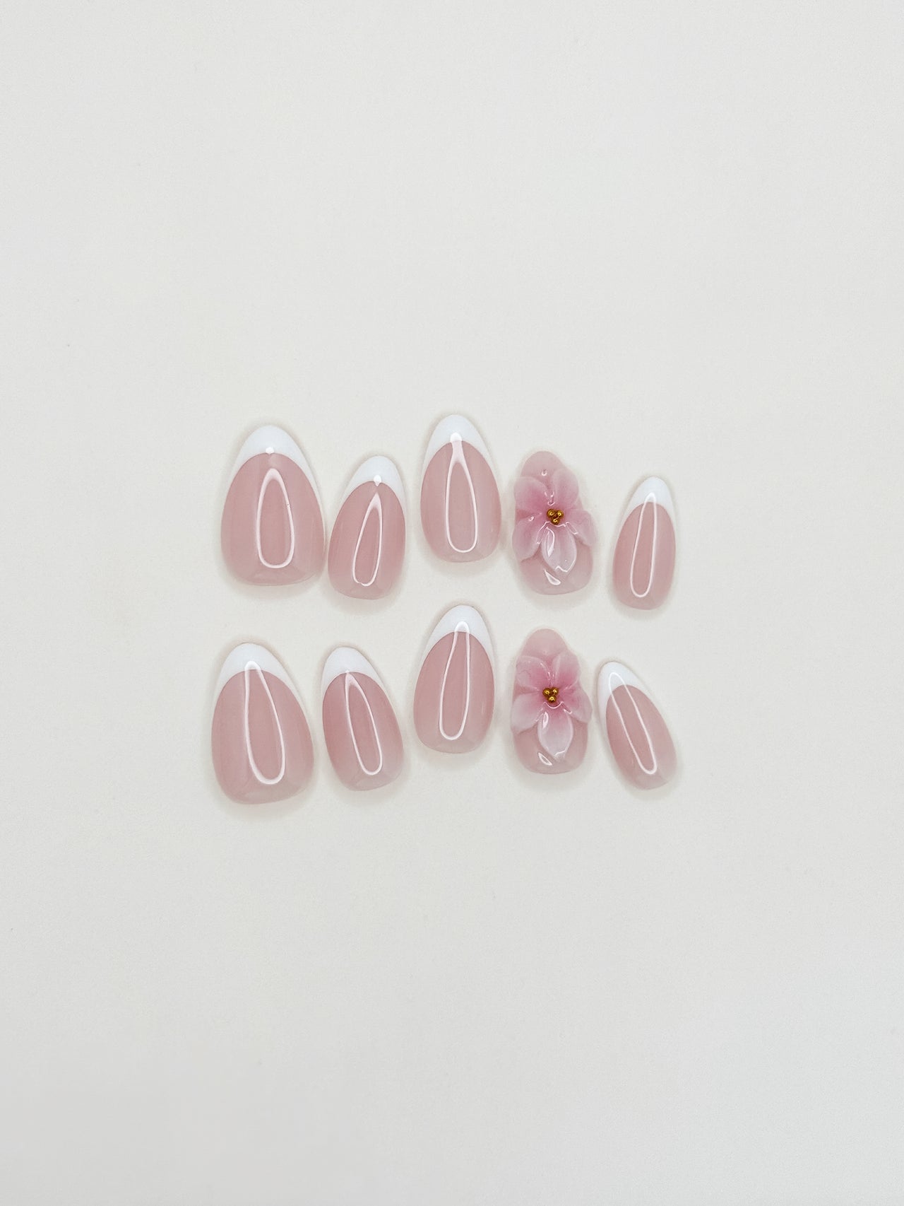 White French tip press-on nails with delicate 3D floral detailing in a glossy medium almond shape. Handmade reusable false nails with a sheer nude pink base inspired by romantic bridal nails, soft feminine manicures and elevated floral French tip designs.