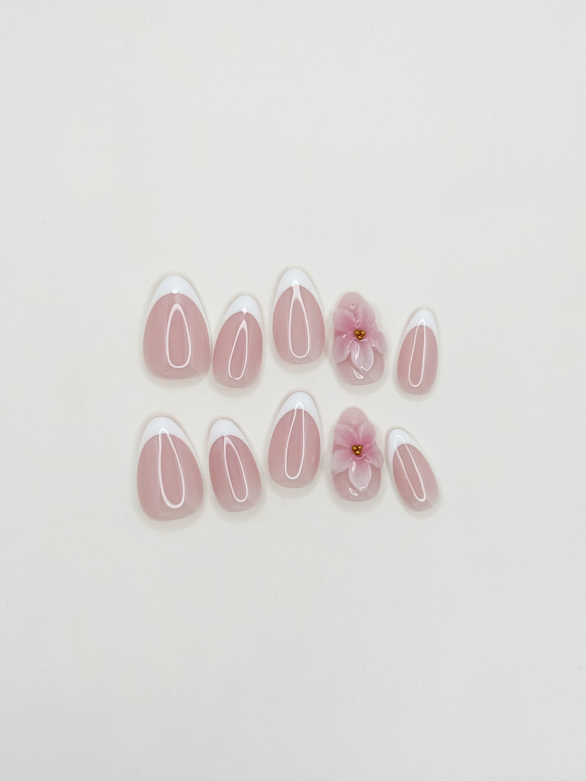 White French tip press-on nails with delicate 3D floral detailing in a glossy medium almond shape. Handmade reusable false nails with a sheer nude pink base inspired by romantic bridal nails, soft feminine manicures and elevated floral French tip designs.