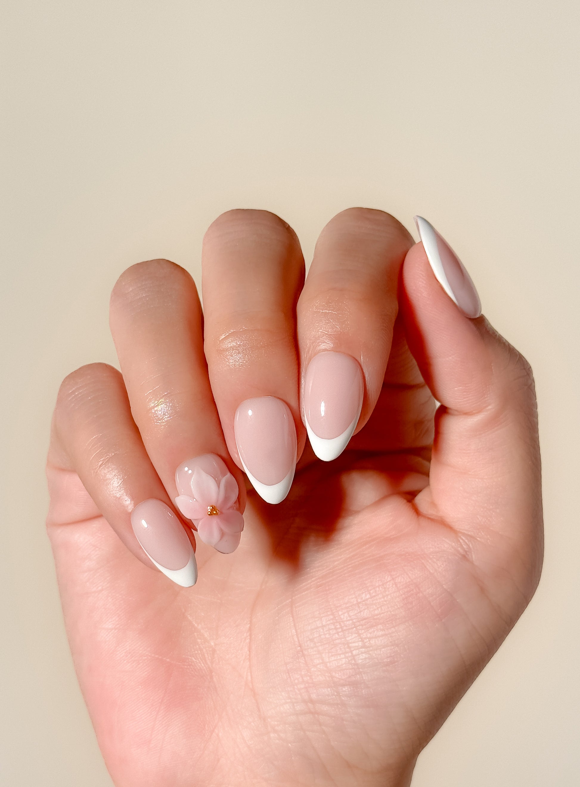 White French tip press-on nails with delicate 3D floral detailing in a glossy medium almond shape. Handmade reusable false nails with a sheer nude pink base inspired by romantic bridal nails, soft feminine manicures and elevated floral French tip designs.