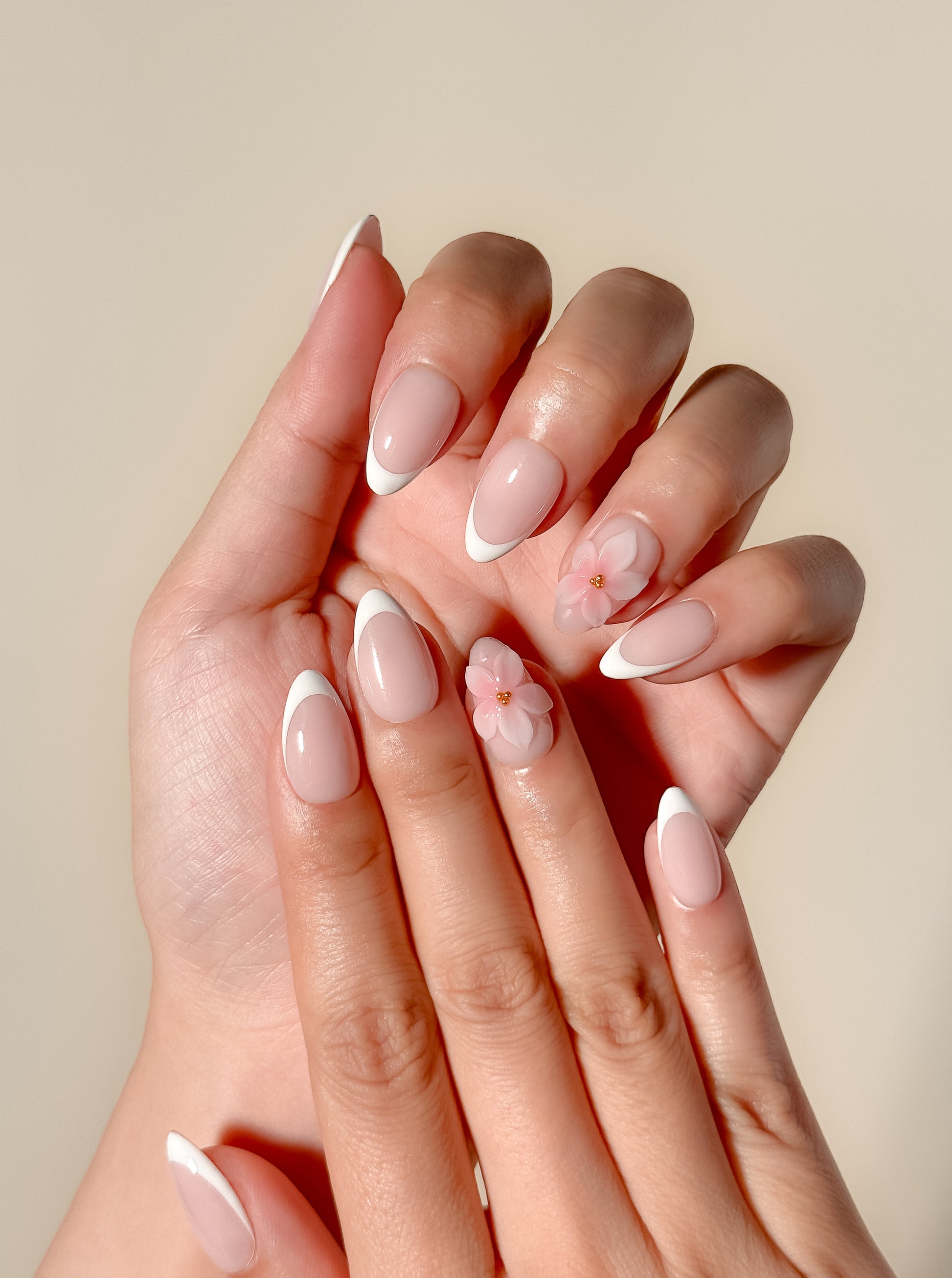 White French tip press-on nails with delicate 3D floral detailing in a glossy medium almond shape. Handmade reusable false nails with a sheer nude pink base inspired by romantic bridal nails, soft feminine manicures and elevated floral French tip designs.