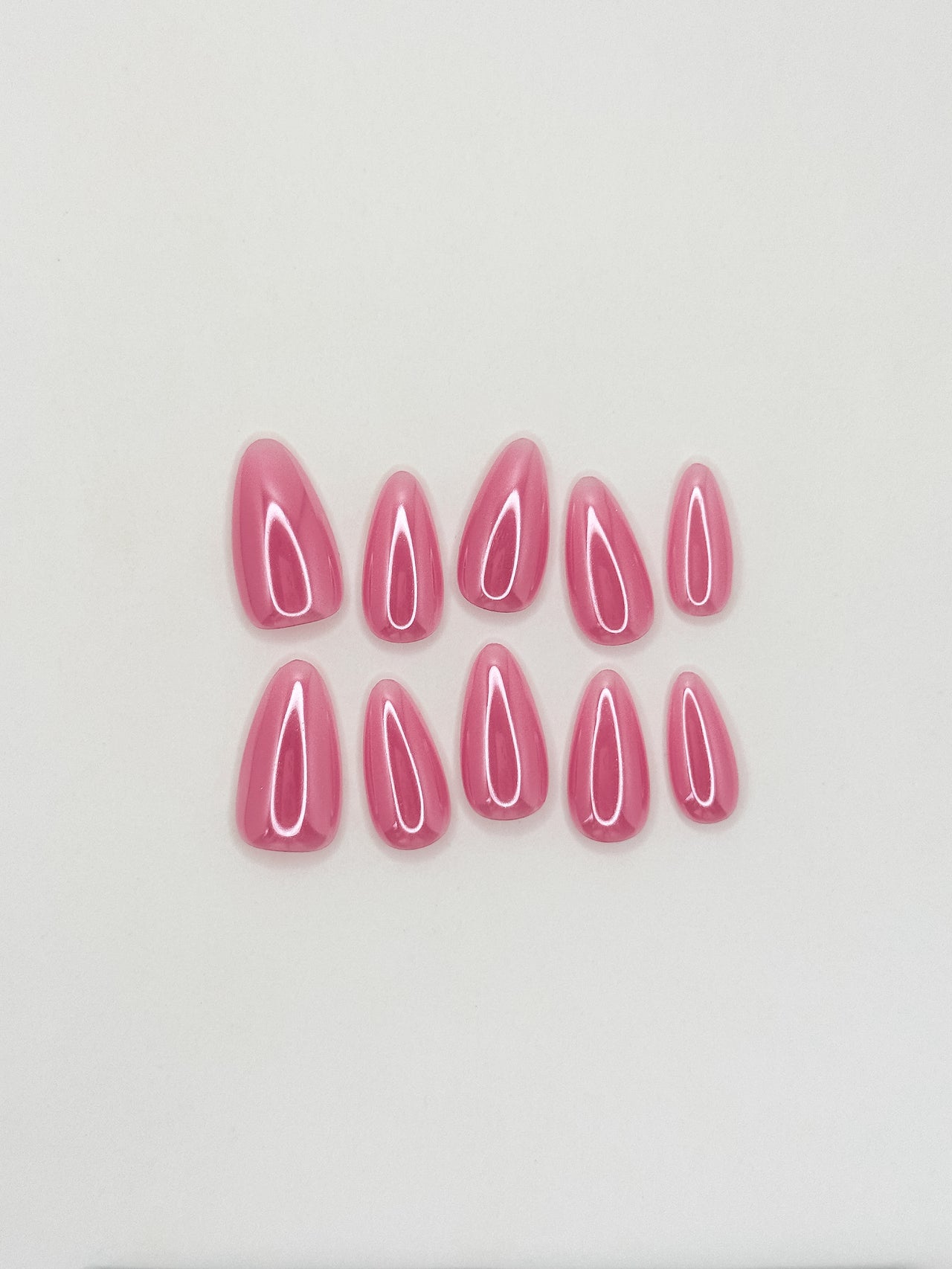 Glossy guava pink glazed press-on nails in a medium almond shape with a translucent tropical finish. Handmade reusable false nails inspired by juicy pink nails, glazed summer manicures and clean girl glossy nail trends.