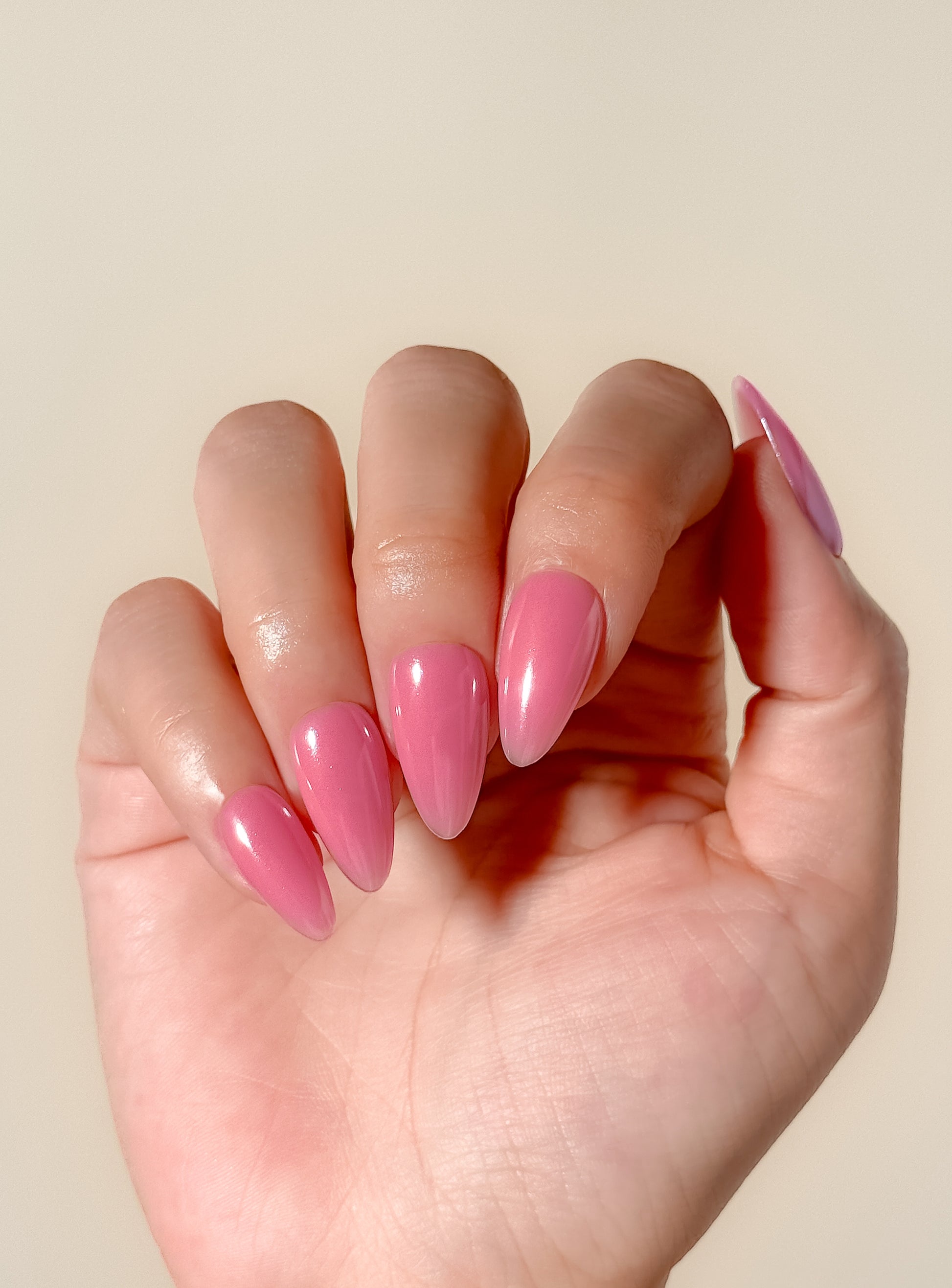 Glossy guava pink glazed press-on nails in a medium almond shape with a translucent tropical finish. Handmade reusable false nails inspired by juicy pink nails, glazed summer manicures and clean girl glossy nail trends.