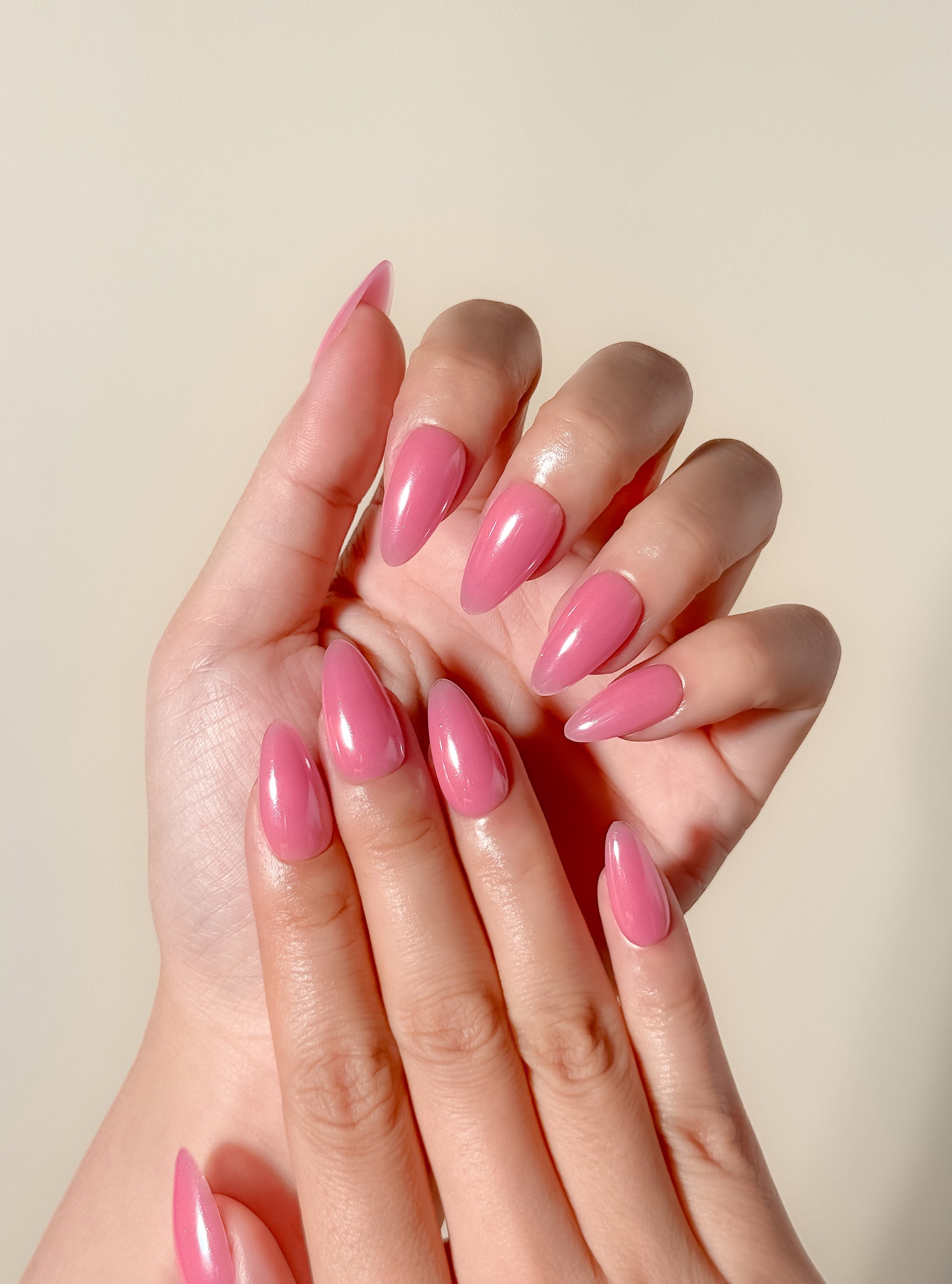 Glossy guava pink glazed press-on nails in a medium almond shape with a translucent tropical finish. Handmade reusable false nails inspired by juicy pink nails, glazed summer manicures and clean girl glossy nail trends.