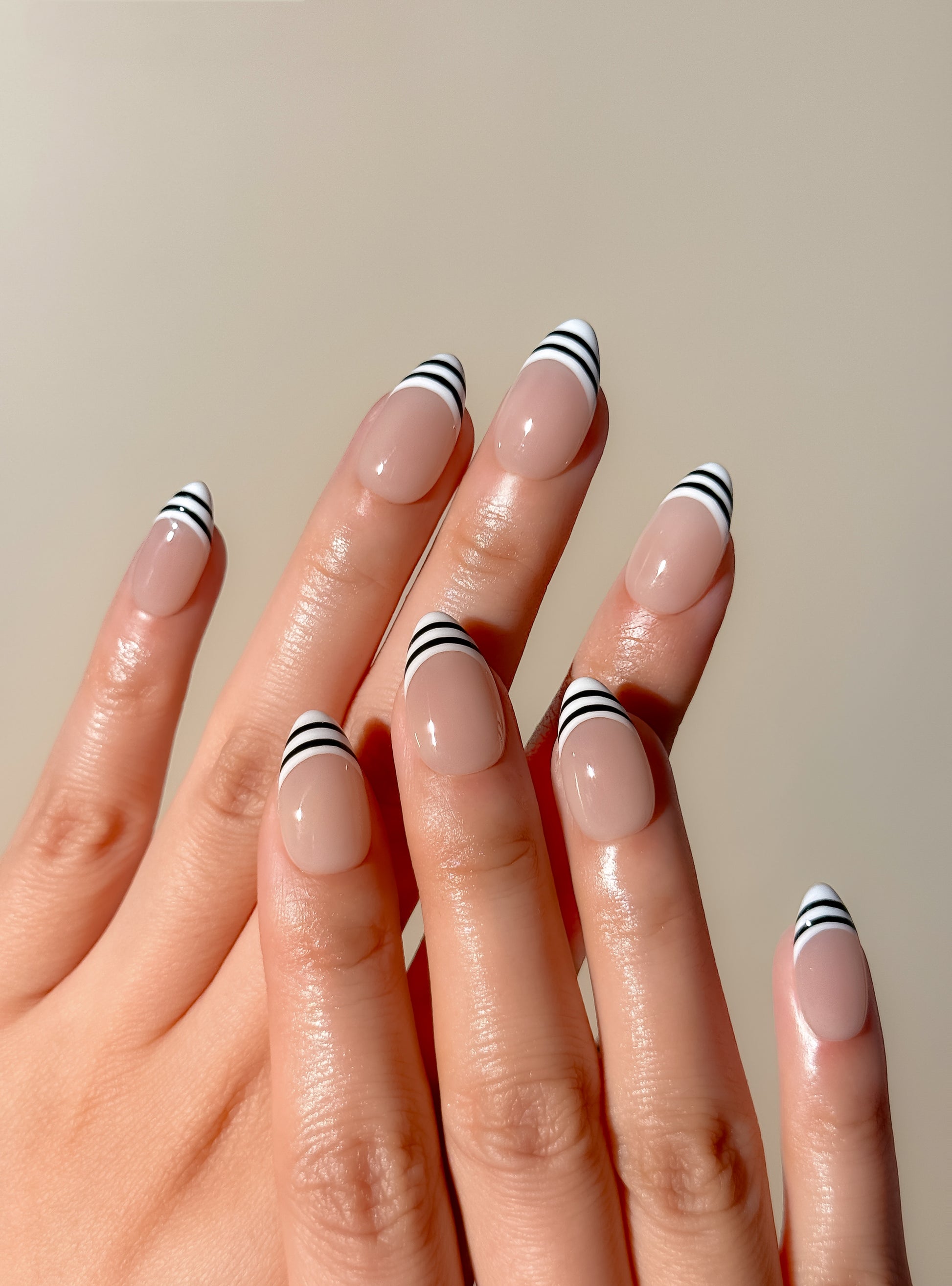 Black and white striped French tip press-on nails in a glossy short almond shape with a sheer nude base. Handmade reusable false nails inspired by graphic French manicure styles, Y2K glam nails and monochrome minimalist nail art.