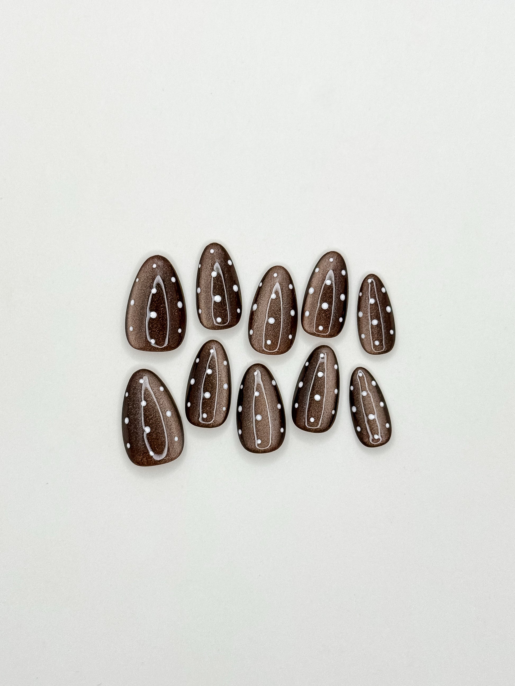 Mocha Dot handmade reusable press-on nails laid flat, featuring glossy brown cat-eye magnetic polish and delicate white polka dot nail art in a medium almond shape.