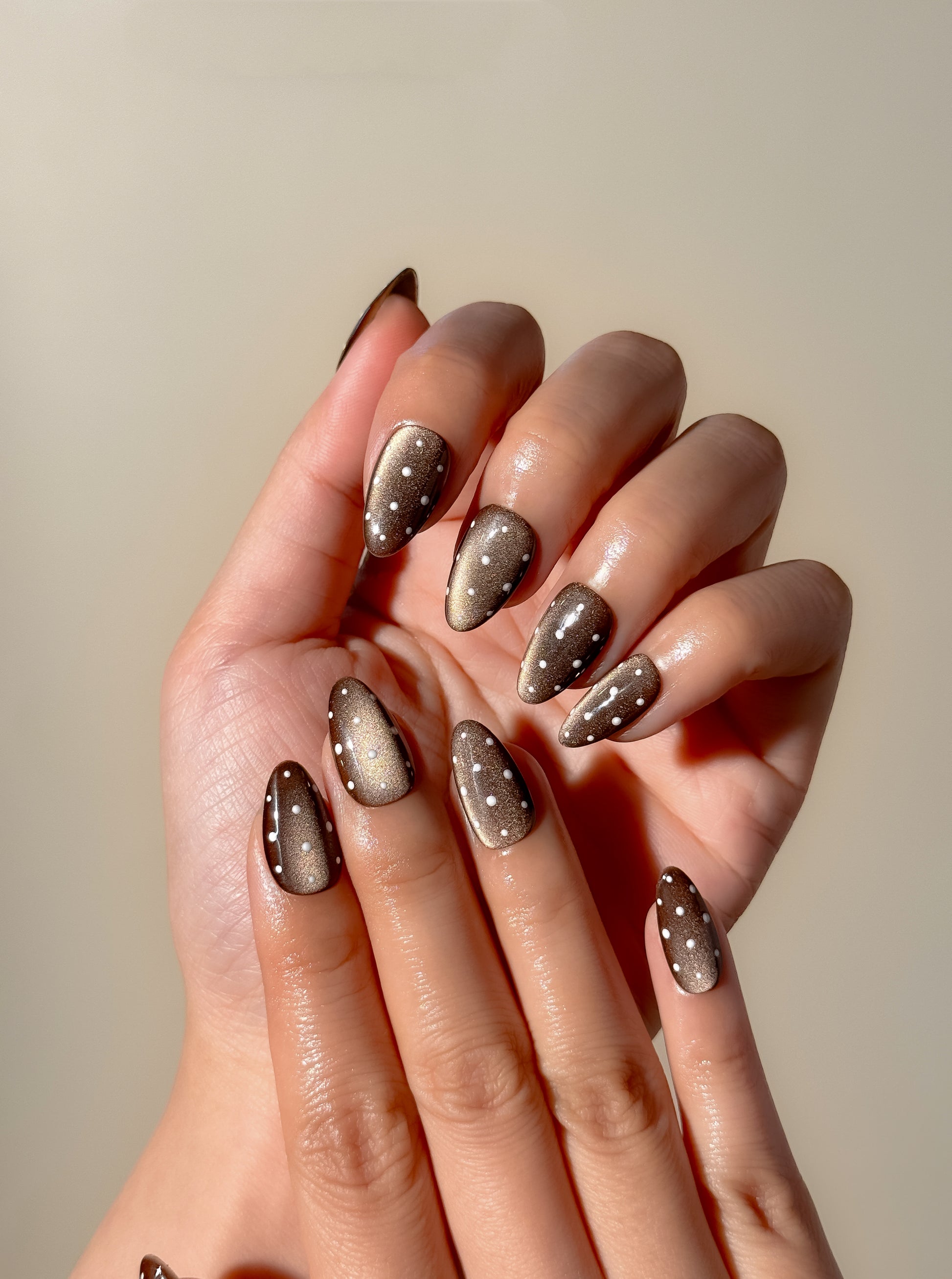 Mocha Dot handmade press-on nails worn on both hands, featuring chocolate brown magnetic cat-eye shine, delicate white dot details and glossy almond-shaped nails.