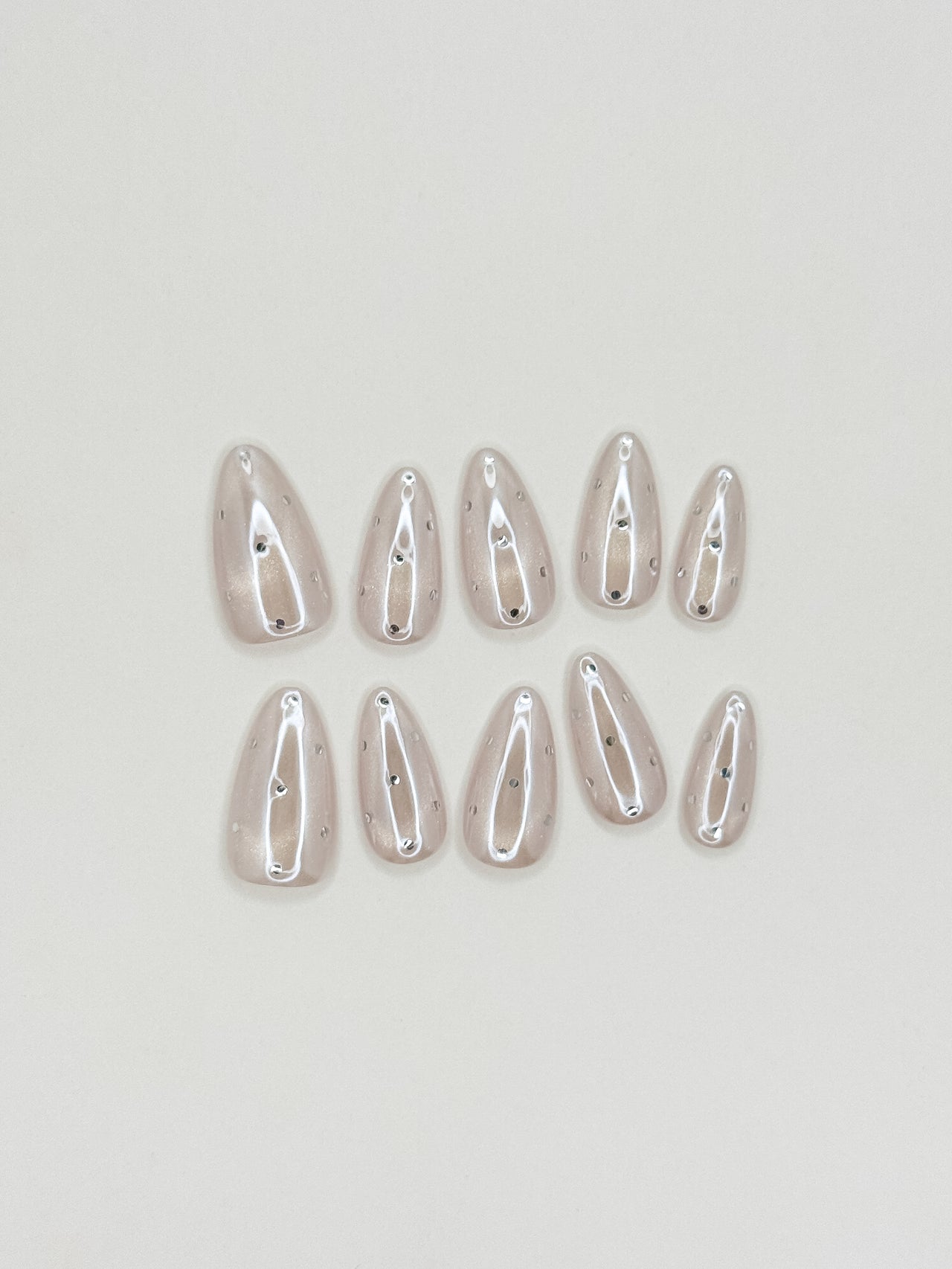 Moon Sugar handmade reusable press-on nails laid flat, featuring a sheer champagne cat-eye finish, soft nude shimmer and tiny silver dot nail art in a medium almond shape.