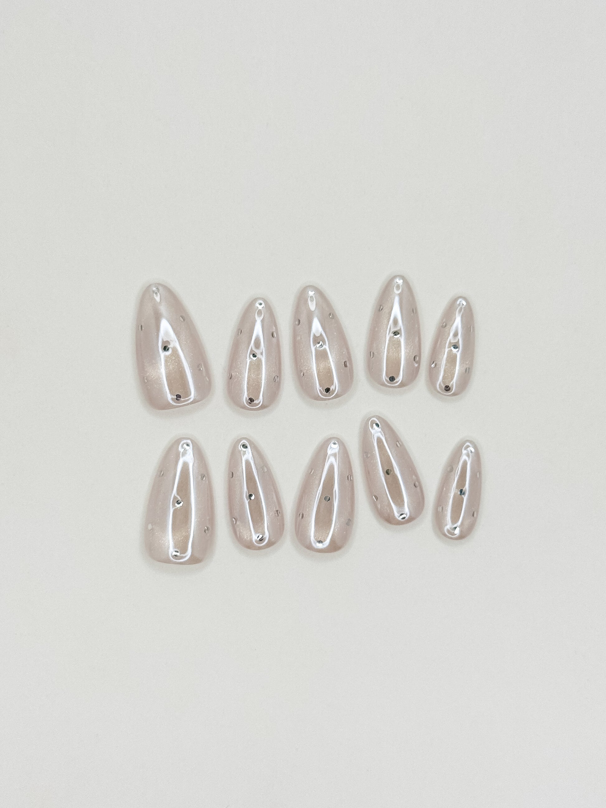 Moon Sugar handmade reusable press-on nails laid flat, featuring a sheer champagne cat-eye finish, soft nude shimmer and tiny silver dot nail art in a medium almond shape.
