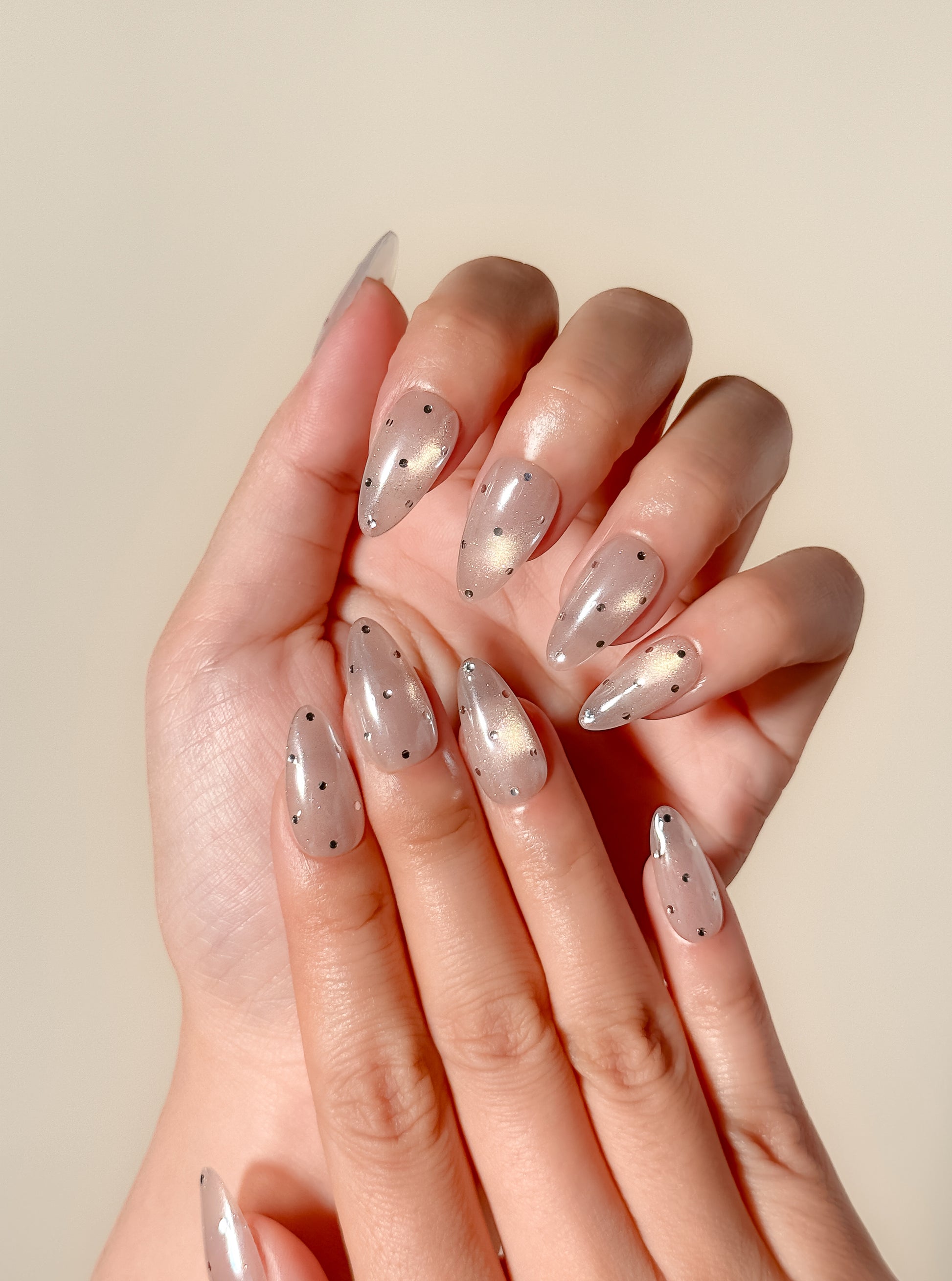 Moon Sugar handmade press-on nails on one hand, featuring sheer nude shimmer, magnetic champagne cat-eye glow and delicate silver celestial dot details.