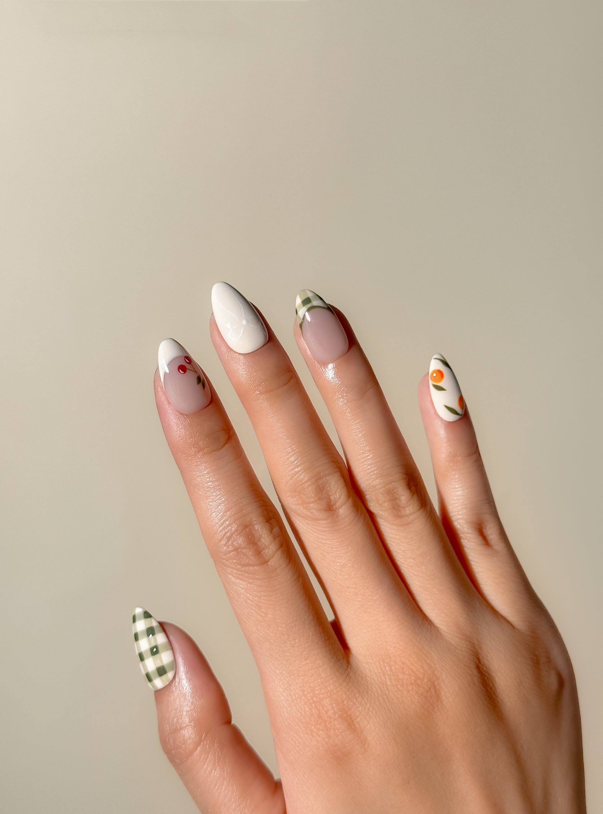 Cream and olive green press-on nails with hand-painted cherry, citrus and gingham French tip detailing in a medium almond shape. Handmade reusable false nails inspired by picnic aesthetics, European summer styling and vintage fruit nail art.