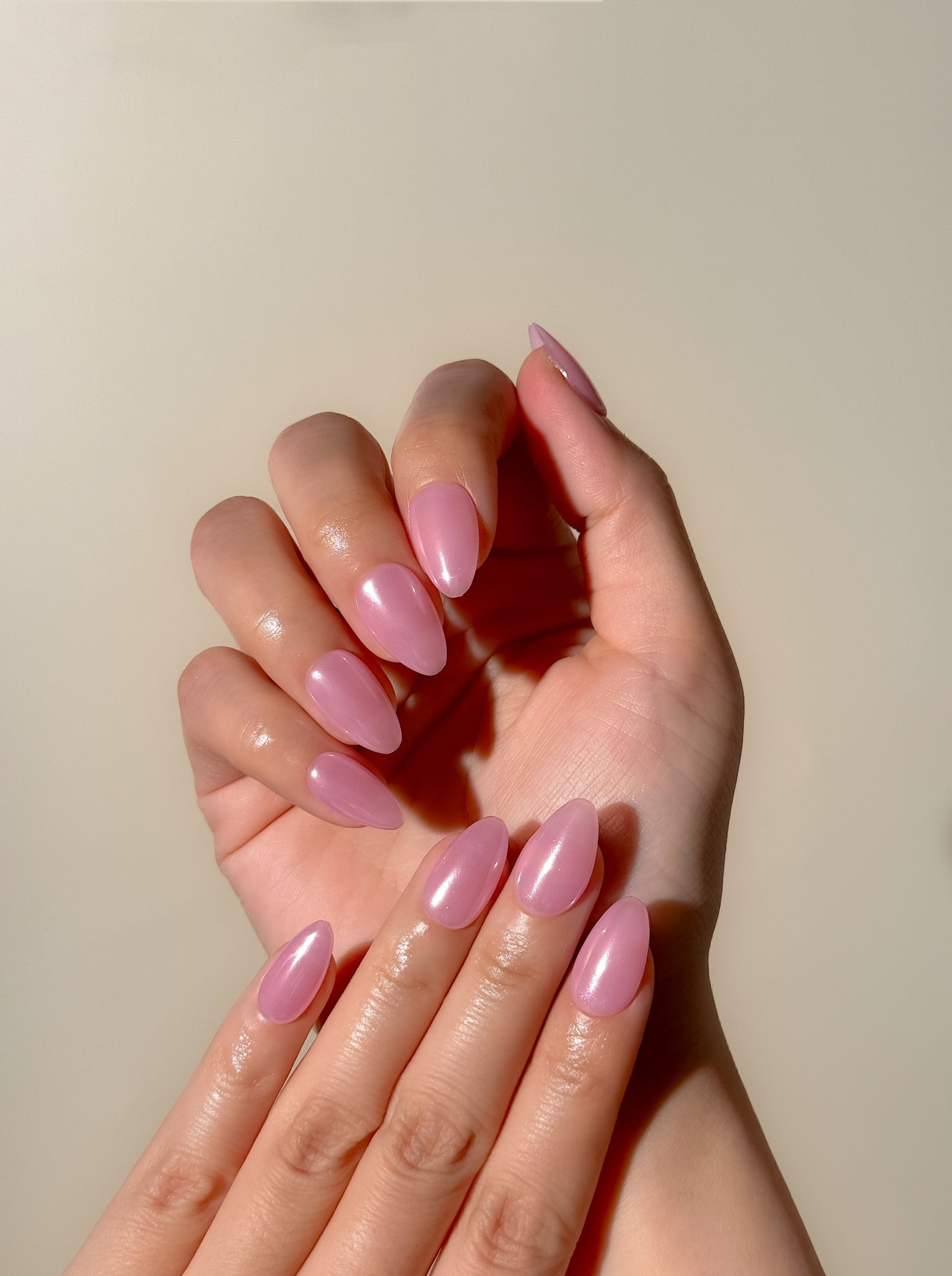 Glossy pink glazed press-on nails in a short almond shape with a translucent candy pink finish. Handmade reusable false nails inspired by glazed donut nails, clean girl manicures and soft glossy pink nail trends.