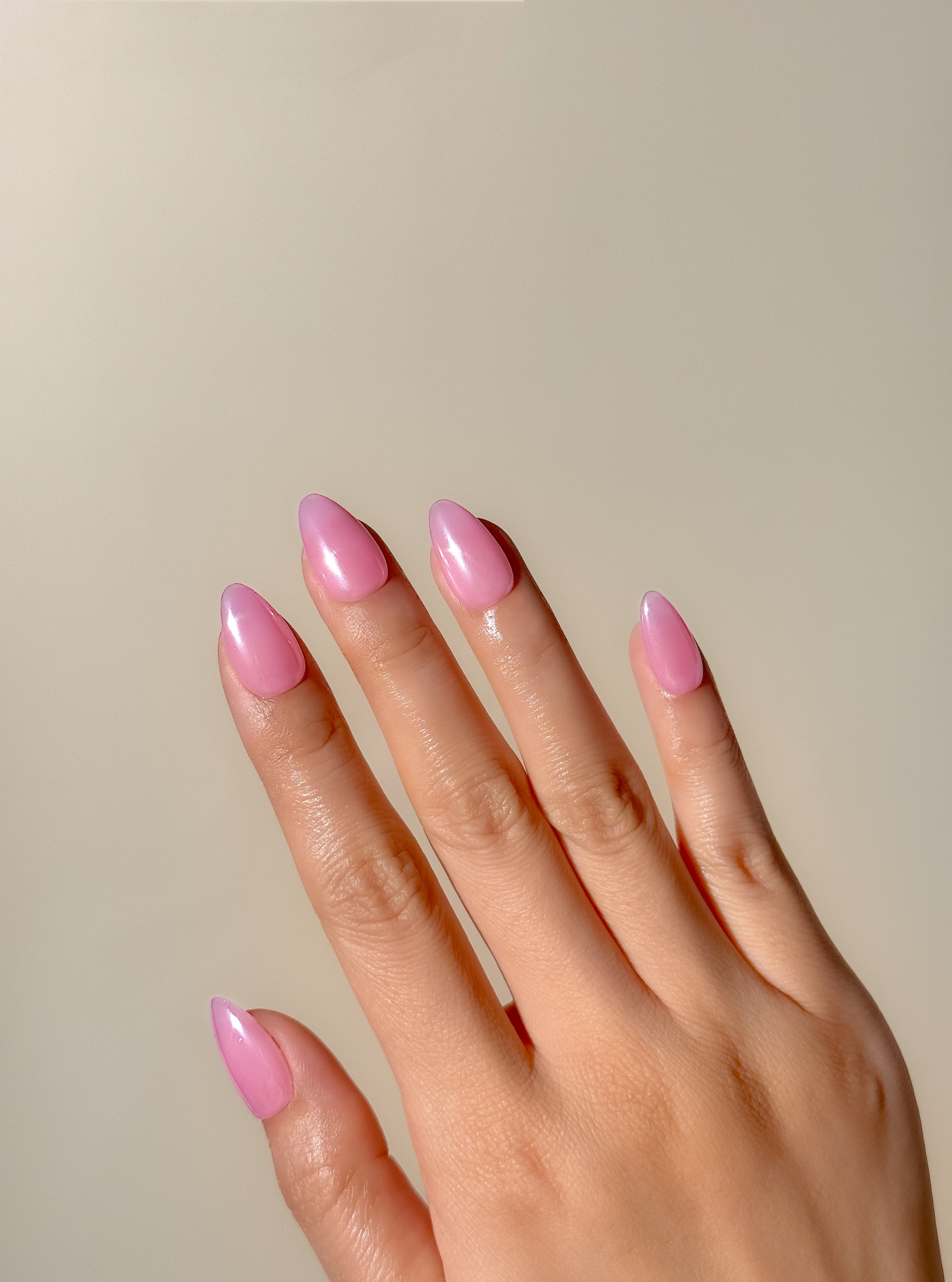 Glossy pink glazed press-on nails in a short almond shape with a translucent candy pink finish. Handmade reusable false nails inspired by glazed donut nails, clean girl manicures and soft glossy pink nail trends.