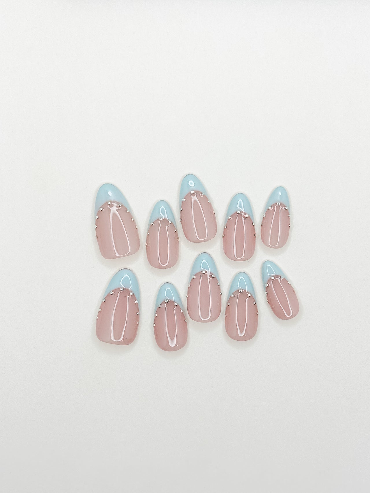 Powder blue French tip press-on nails with silver stud detailing in a glossy medium almond shape. Handmade reusable false nails with a sheer nude pink base inspired by European Riviera summer style and soft glam French manicure trends.