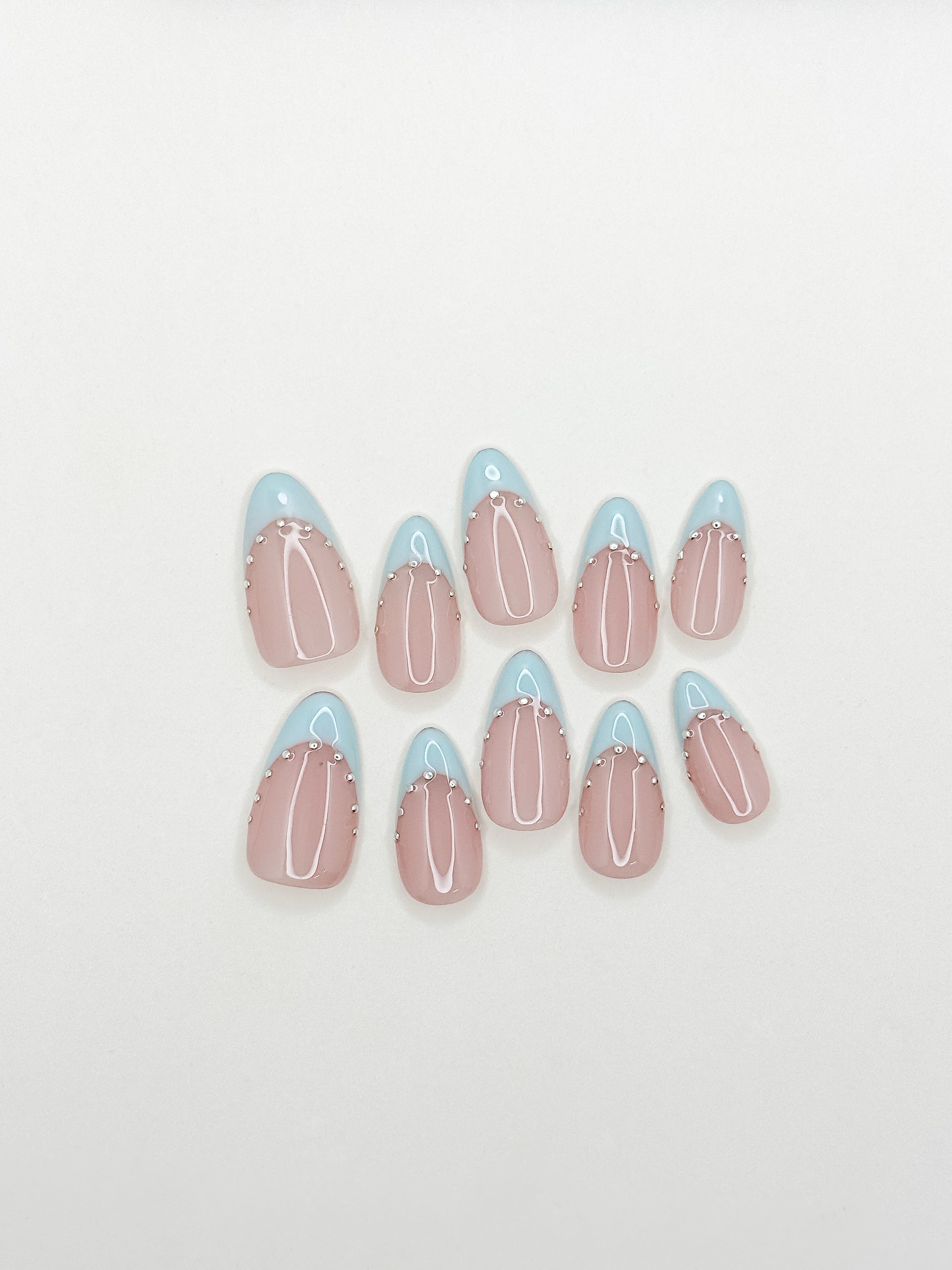 Powder blue French tip press-on nails with silver stud detailing in a glossy medium almond shape. Handmade reusable false nails with a sheer nude pink base inspired by European Riviera summer style and soft glam French manicure trends.