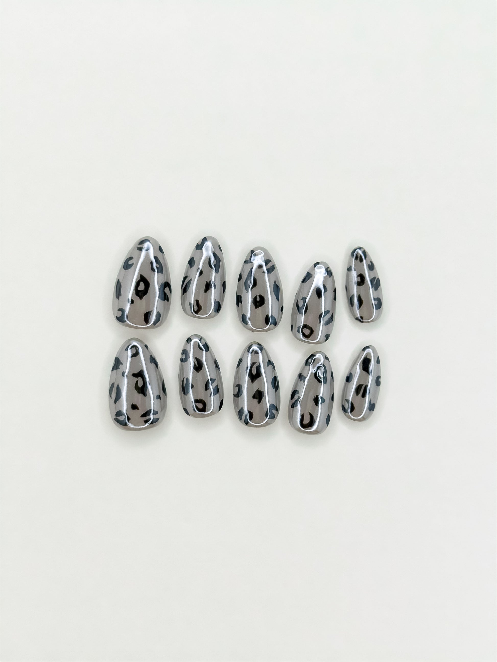 Roadie handmade short almond press-on nails arranged on white, featuring reflective silver chrome and black leopard-print spots.