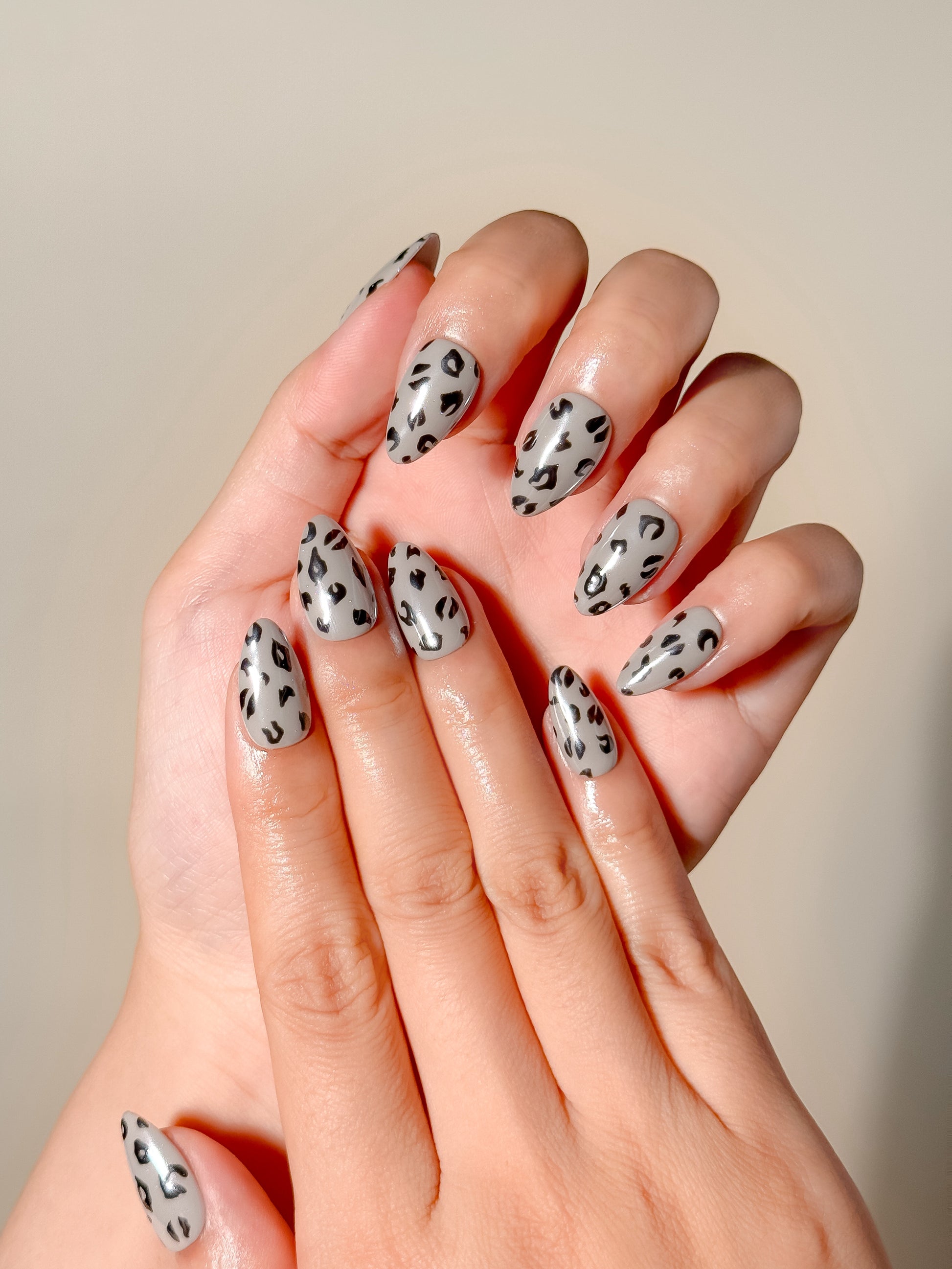 Roadie handmade animal-print press-on nails worn on two hands, with reflective silver bases and hand-painted black leopard spots.