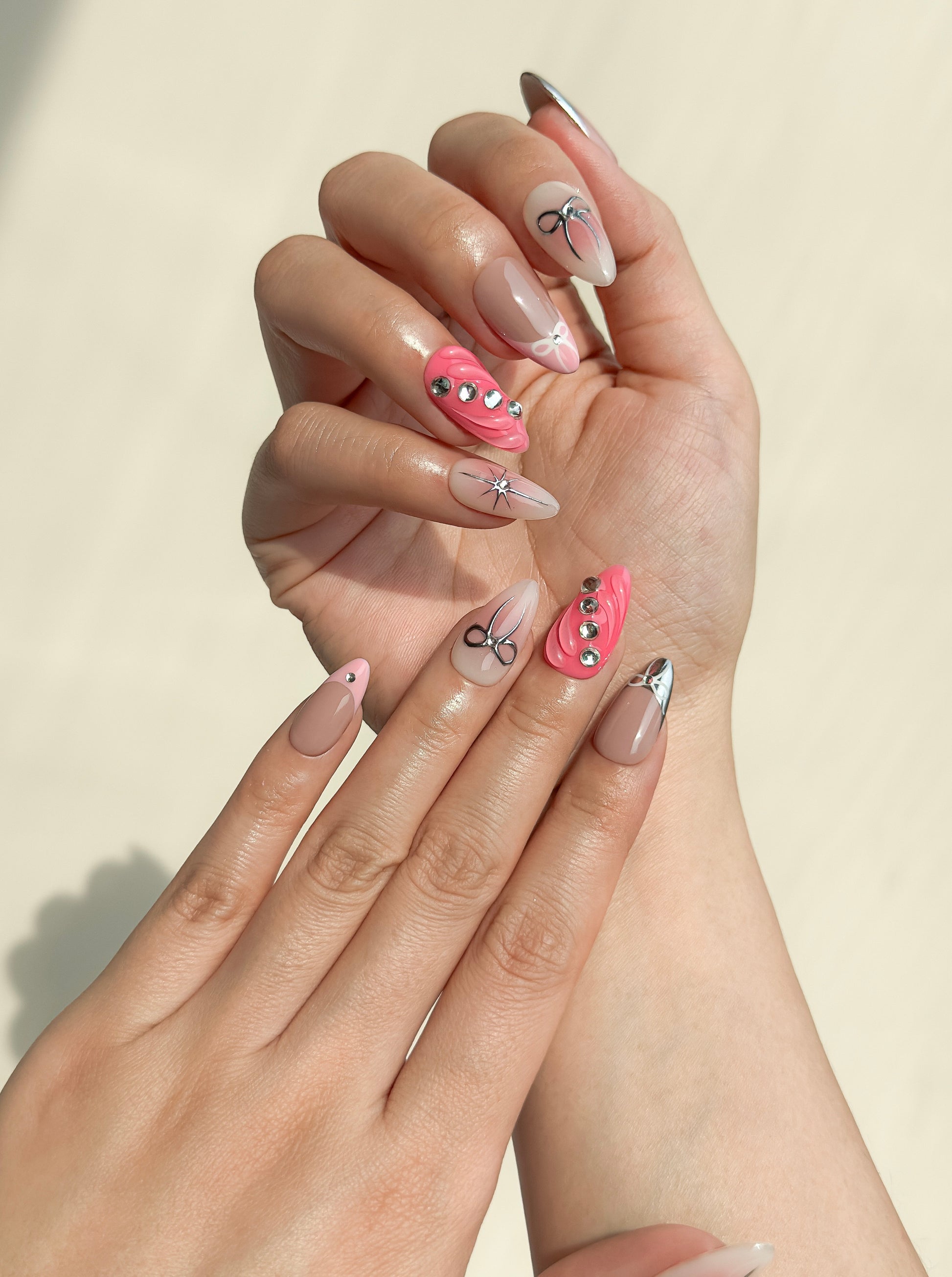 Starlit press-on nails worn on both hands, showing glossy nude bases, chrome silver French tips, bow nail art, starburst accents and bright pink 3D statement nails.