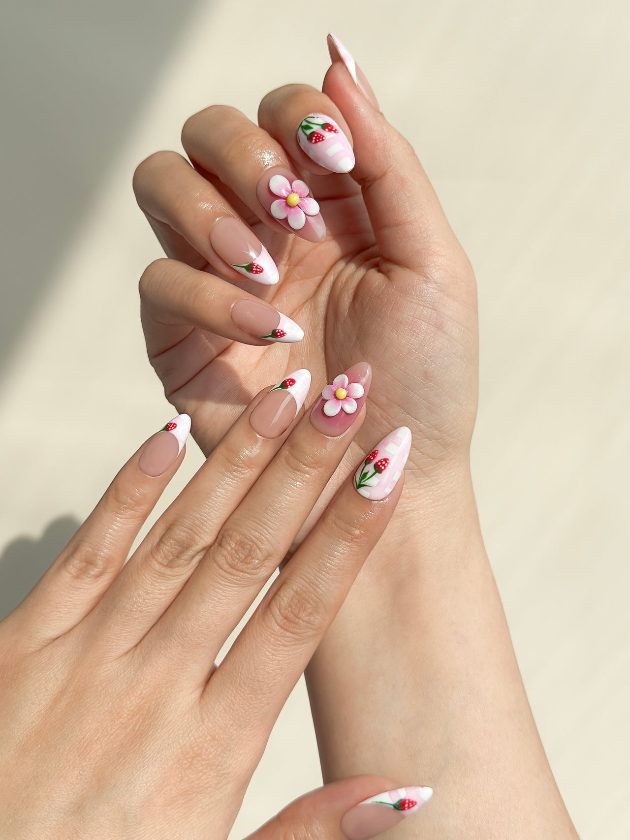 Strawberry Dream handmade reusable press-on nails laid flat, featuring sheer nude bases, pink gingham French tips, hand-painted strawberry details and raised 3D flower accents in a medium almond shape.